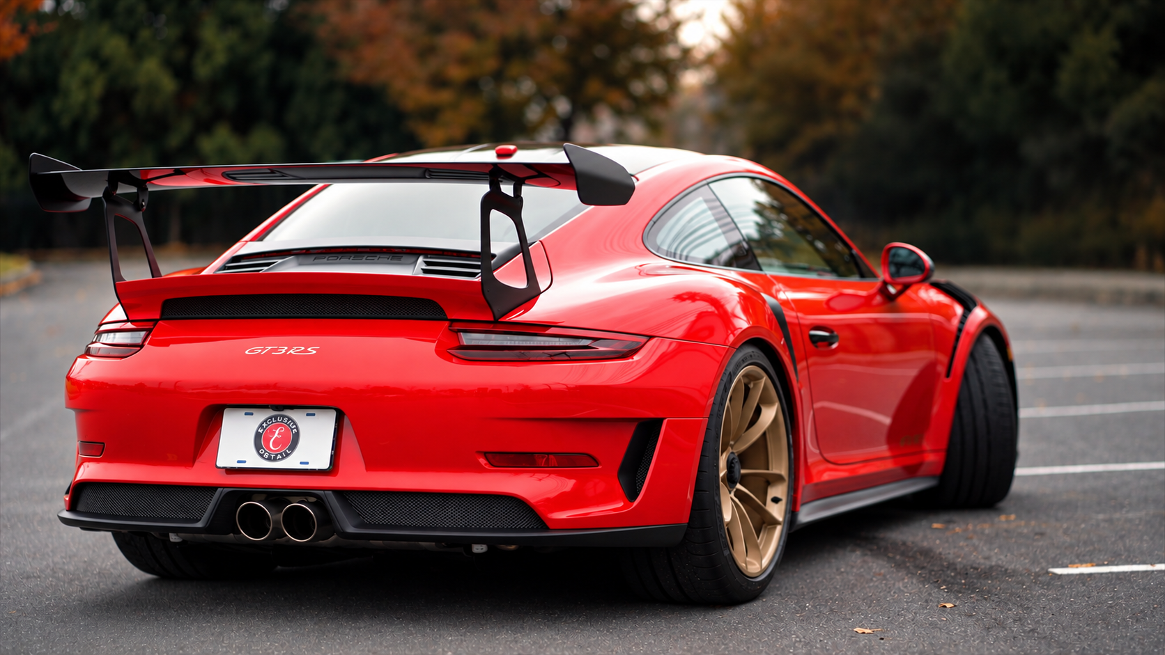 Red Porsche sports car with a large rear wing, parked on an empty parking lot with trees in the background.