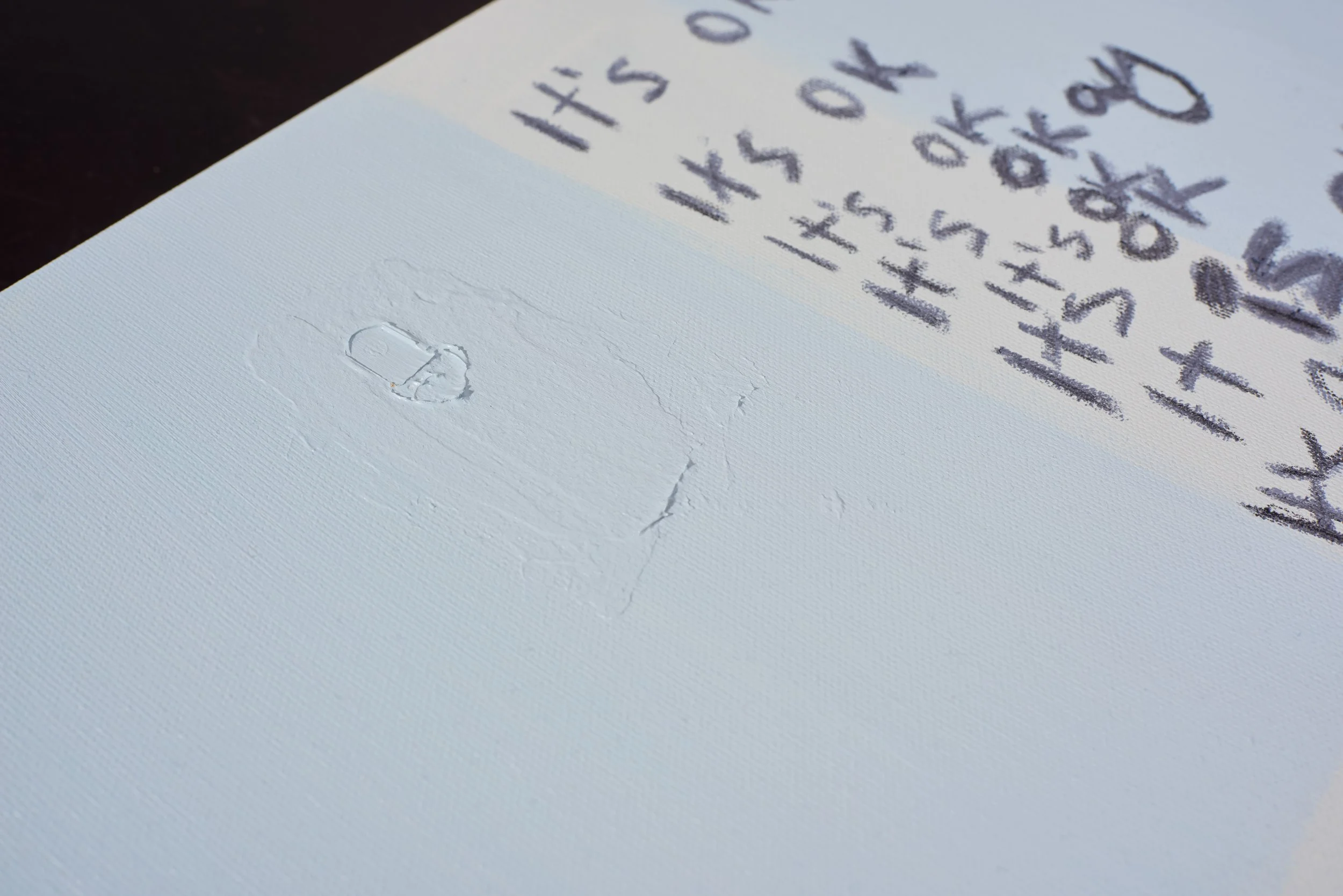 A close-up view of a white textured sheet of paper with handwritten text in dark ink, and an imprint of an eraser or correction tool on the lower left side.