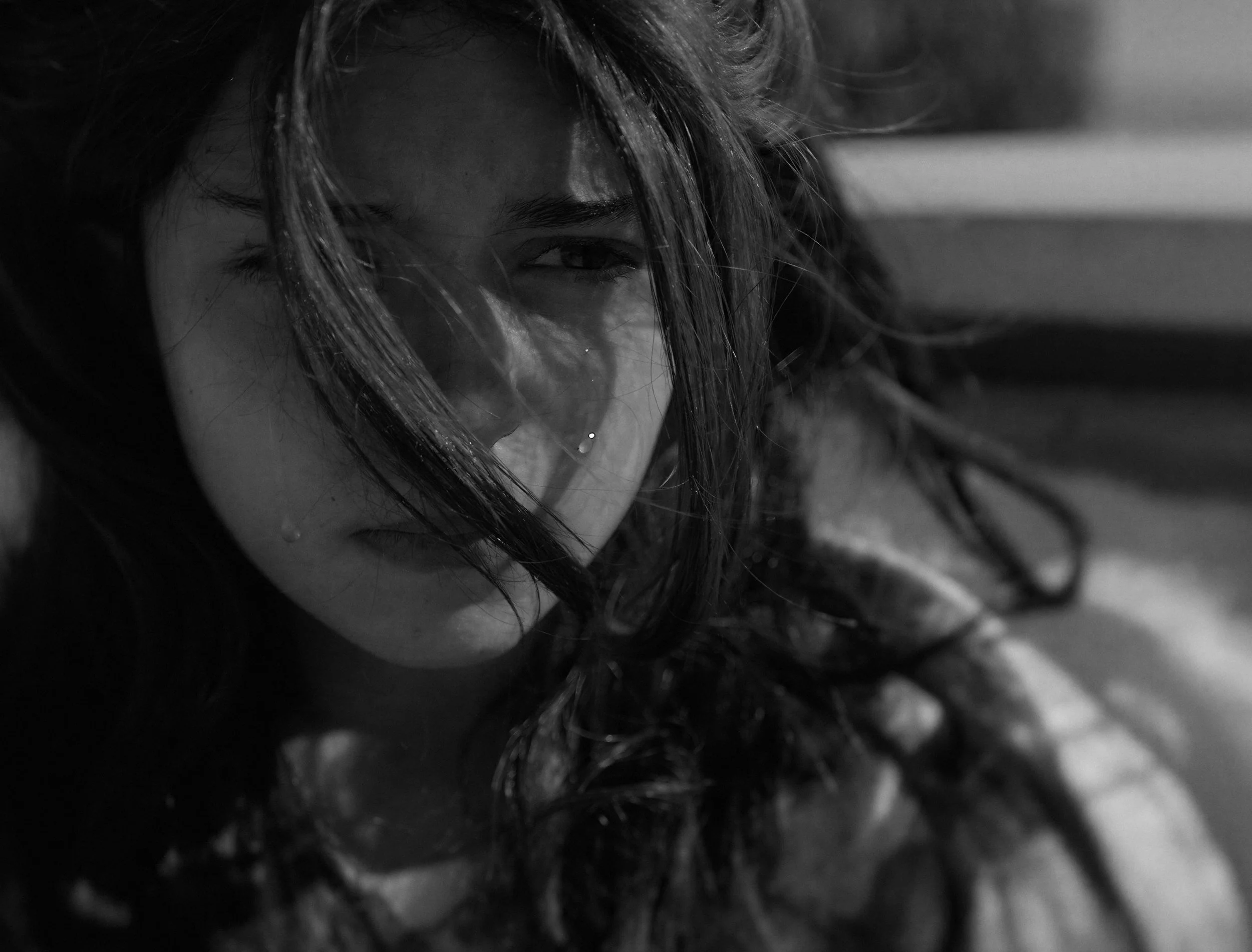 Close-up of a woman's face with wet hair partially covering her face, black and white photo.