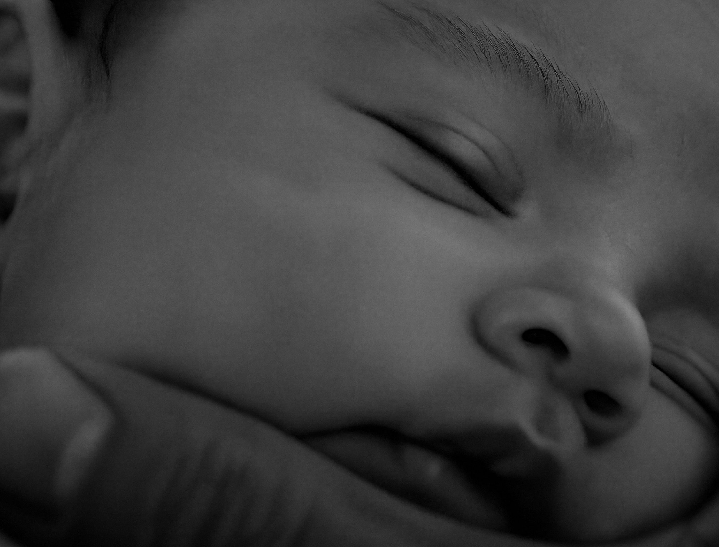 Close-up of a person's face, showing one closed eye, brow, and part of the nose in black and white.