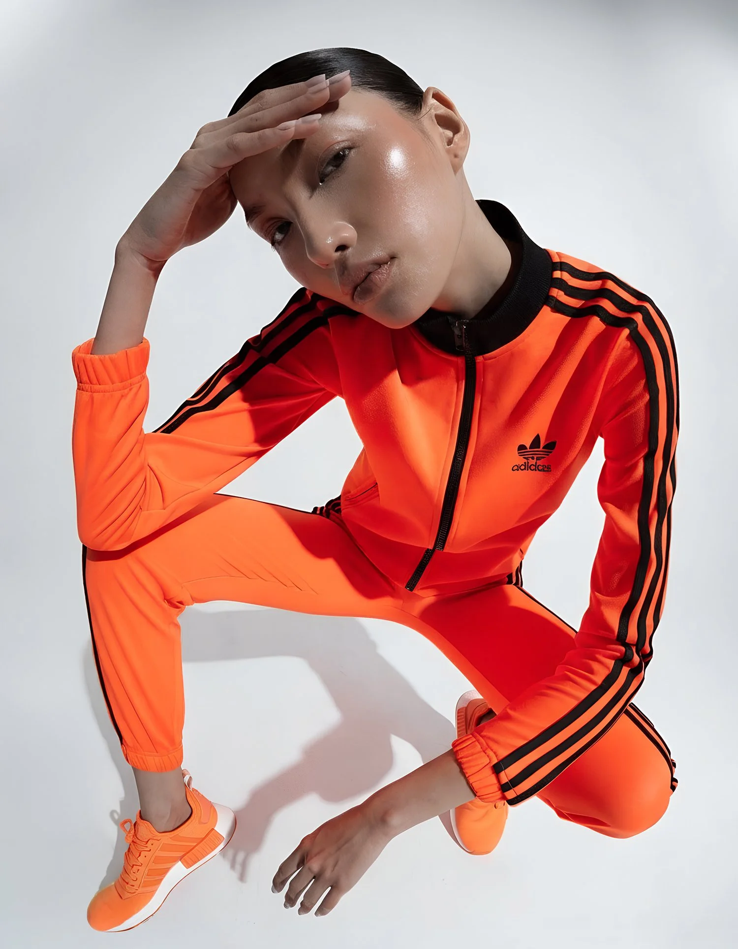 A person in an orange Adidas tracksuit with black stripes posing against a white background.
