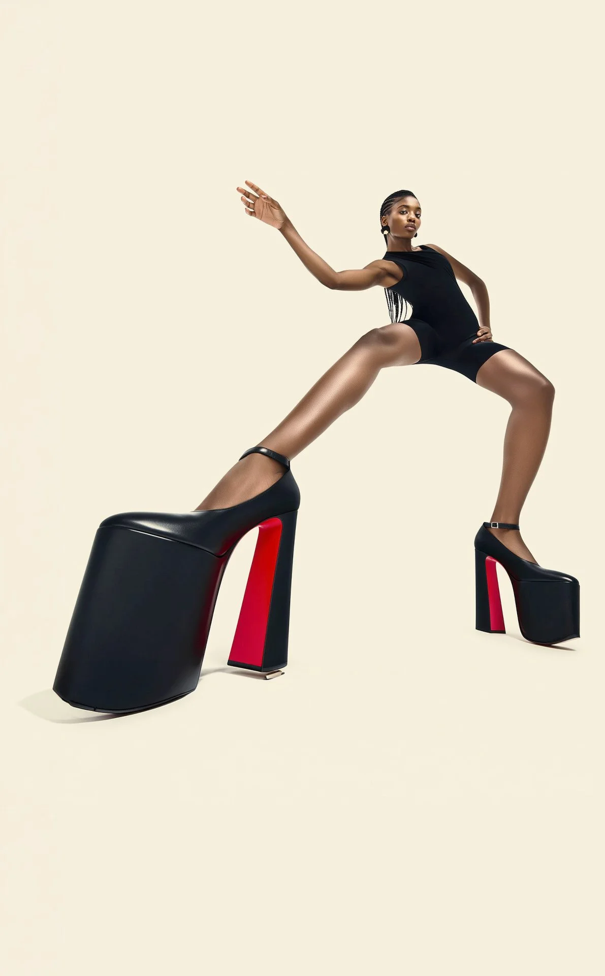 A woman with dark skin posing in a black outfit and high heel shoes with red soles, standing with one leg on a large black platform heel and stretching her arm outward against a plain light background.