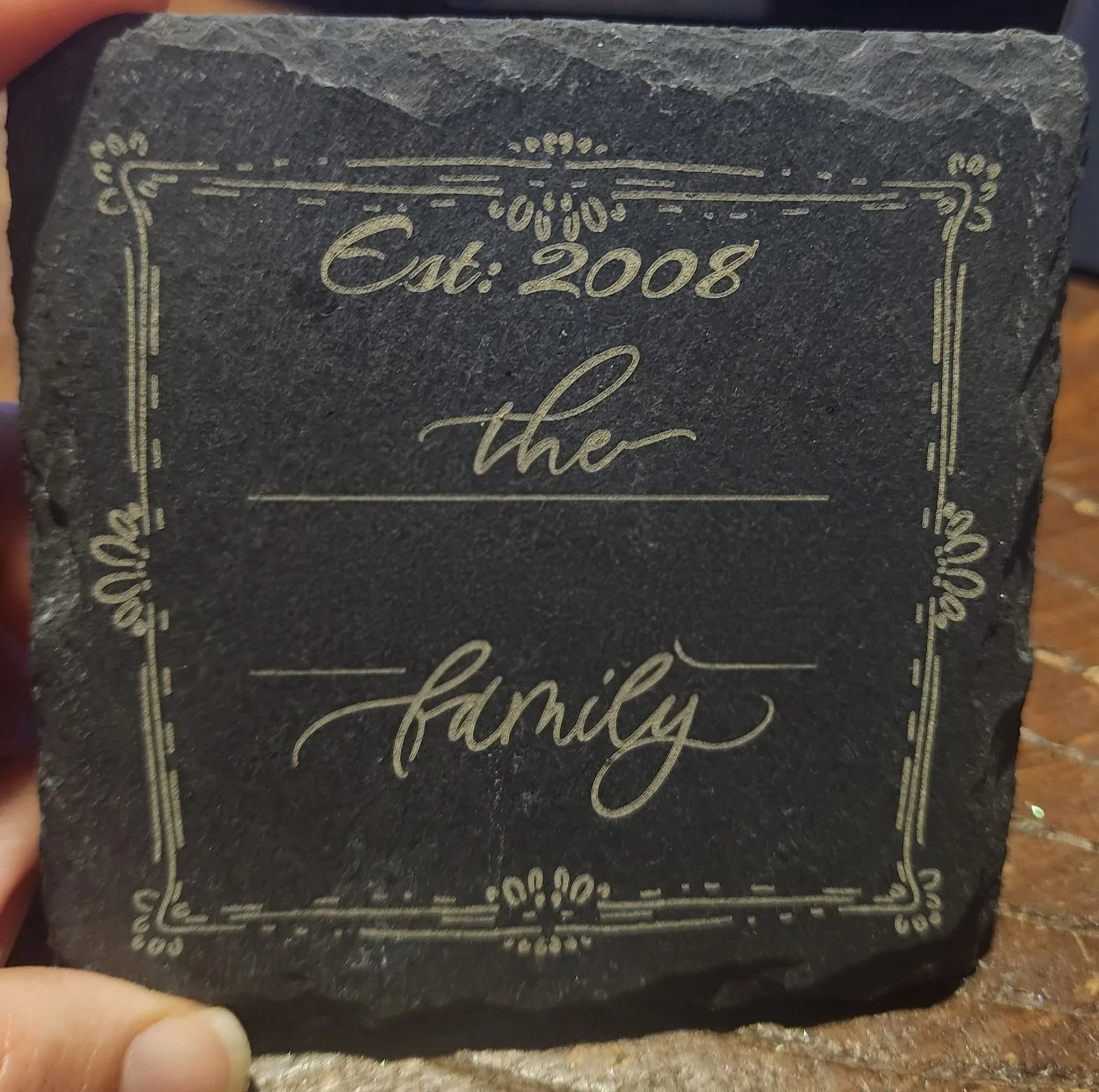 Close-up of a black cake with gold decorative writing and designs, including the words 'Est. 2008'.