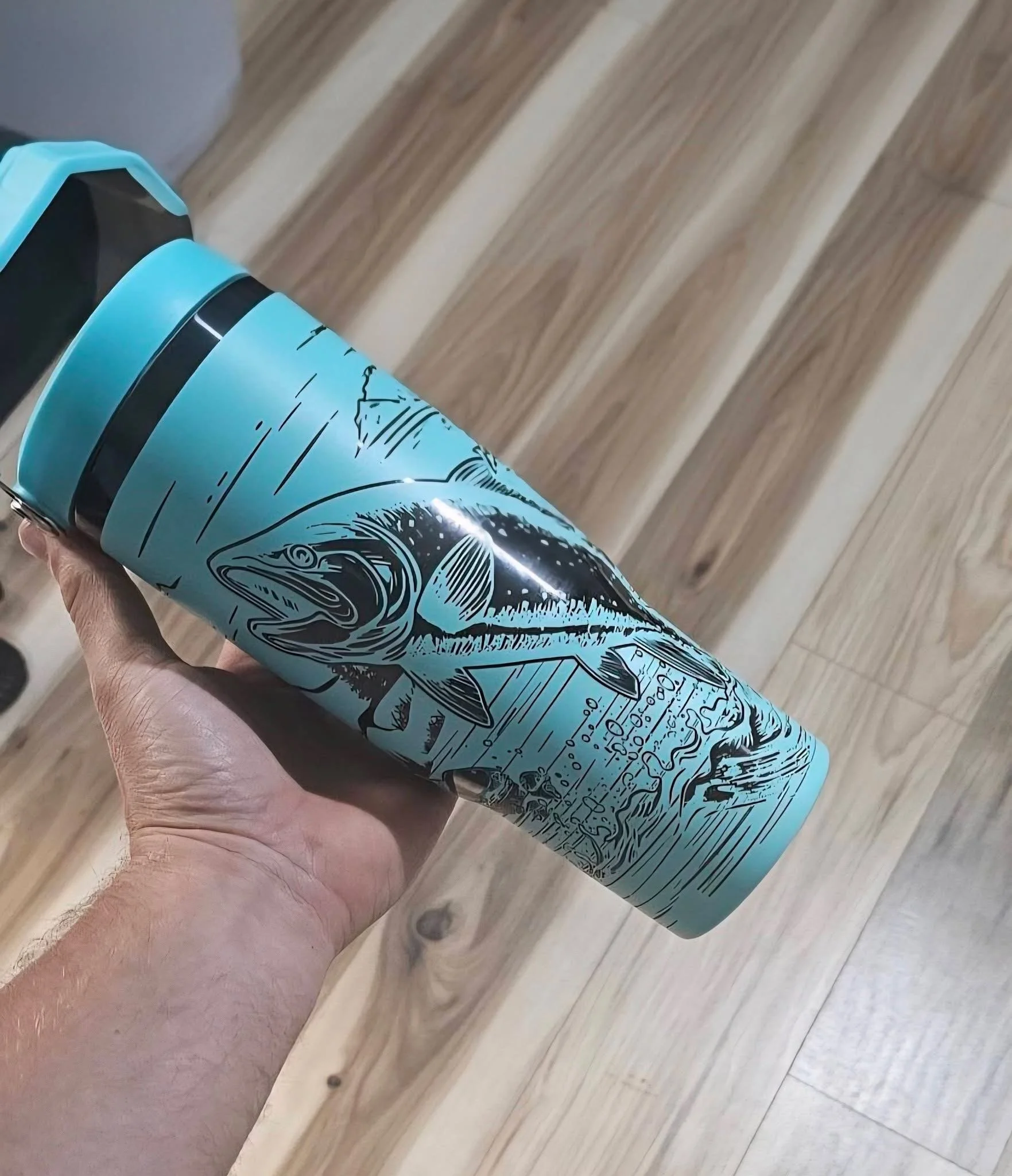 A person holding a can of Aquaman-themed beer with a fish illustration, standing on wooden flooring.