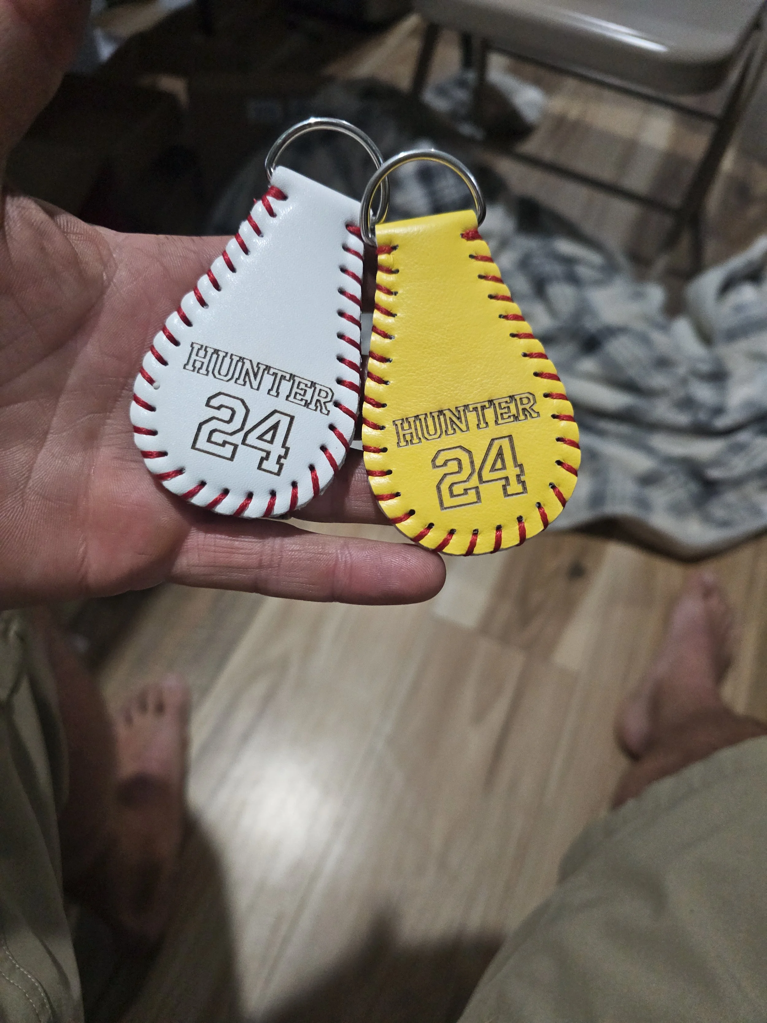 Close-up of two keychains resembling sneakers, one white and one yellow, both with red stitching and 'HUNTER 24' printed on them, held by a person's hand.Custom sports-themed keychains with personalized designs
