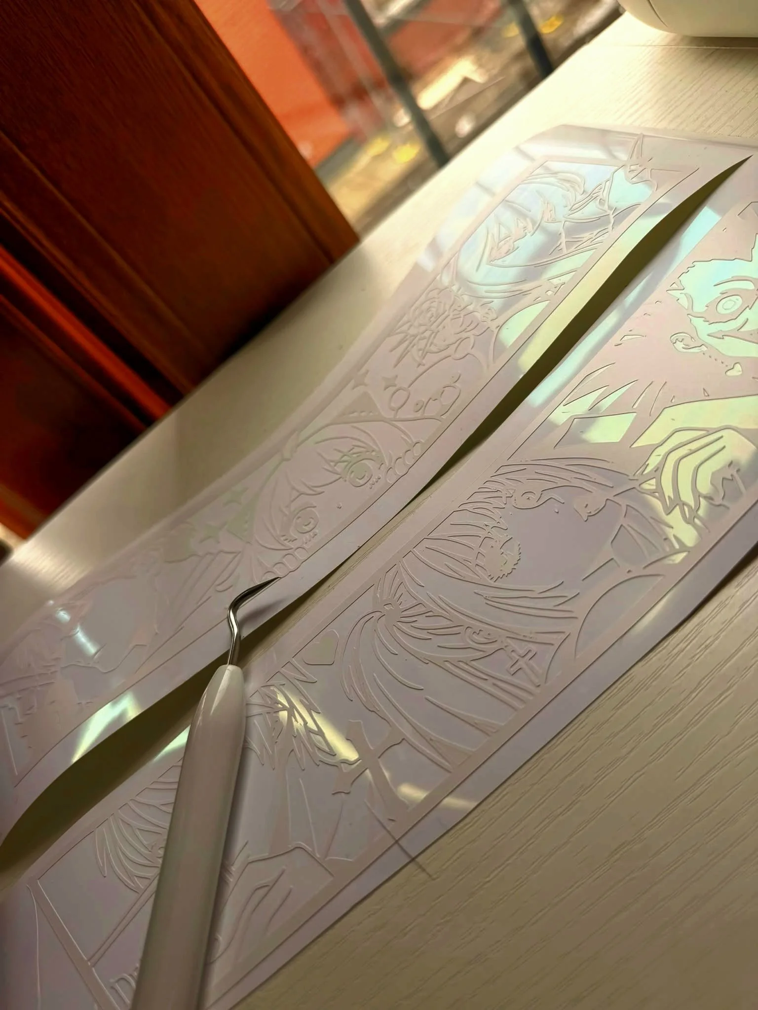 Close-up of a metallic tool on top of intricately cut paper art with images of a superhero and other detailed designs.