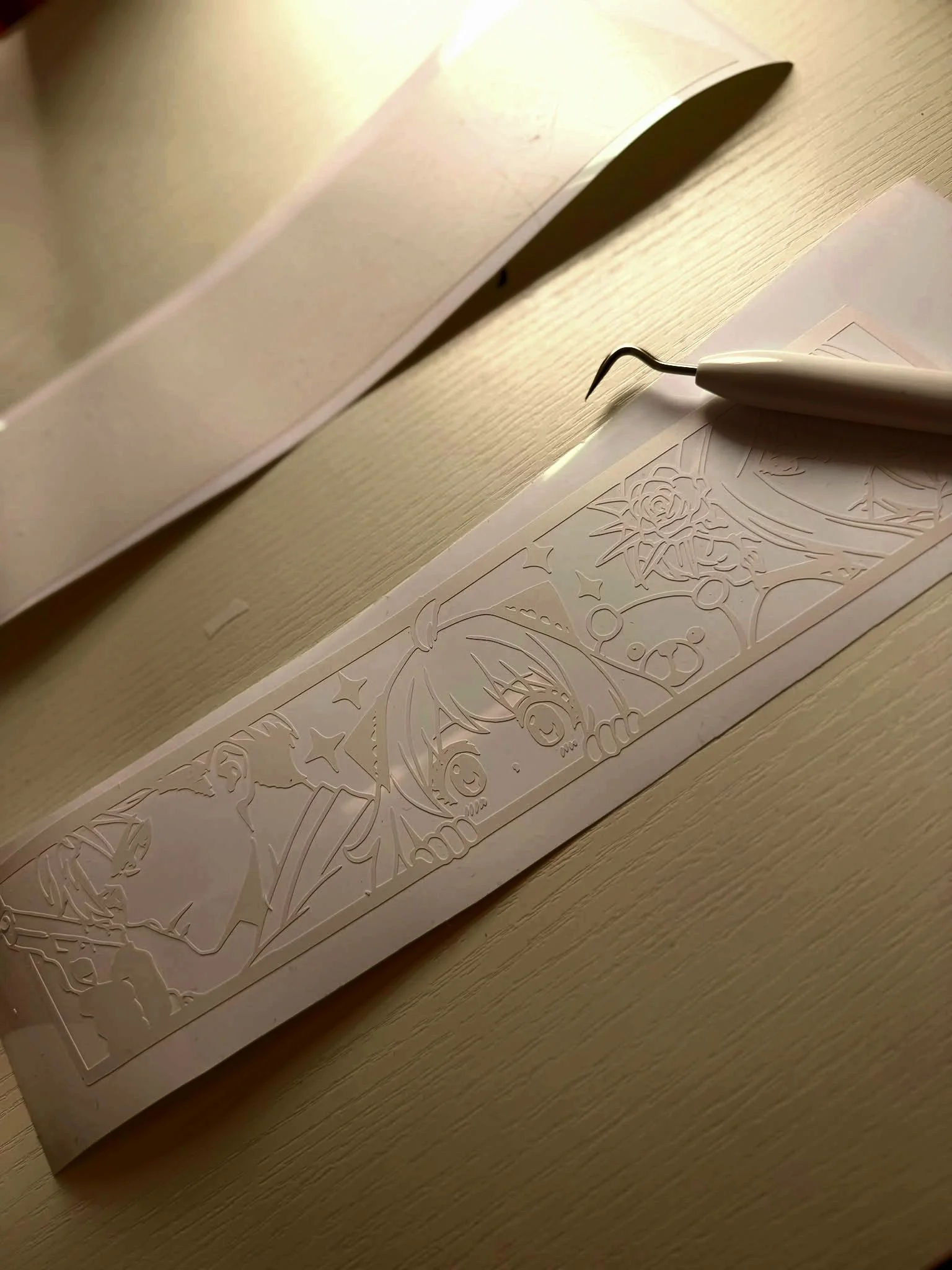 Unfinished white paper craft with cut-out intricate design, featuring a festive theme with snowflakes, stars, and ornaments, resting on a wooden surface, with a precision craft tool nearby.
