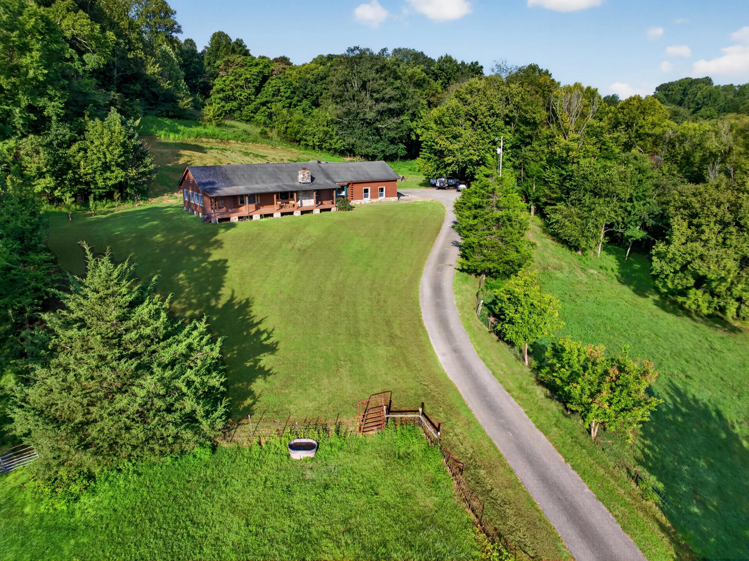 Arial view of Refuge Ranch surrounded by mature trees and rolling green hills, with the winding driveway leading to the secluded retreat.
