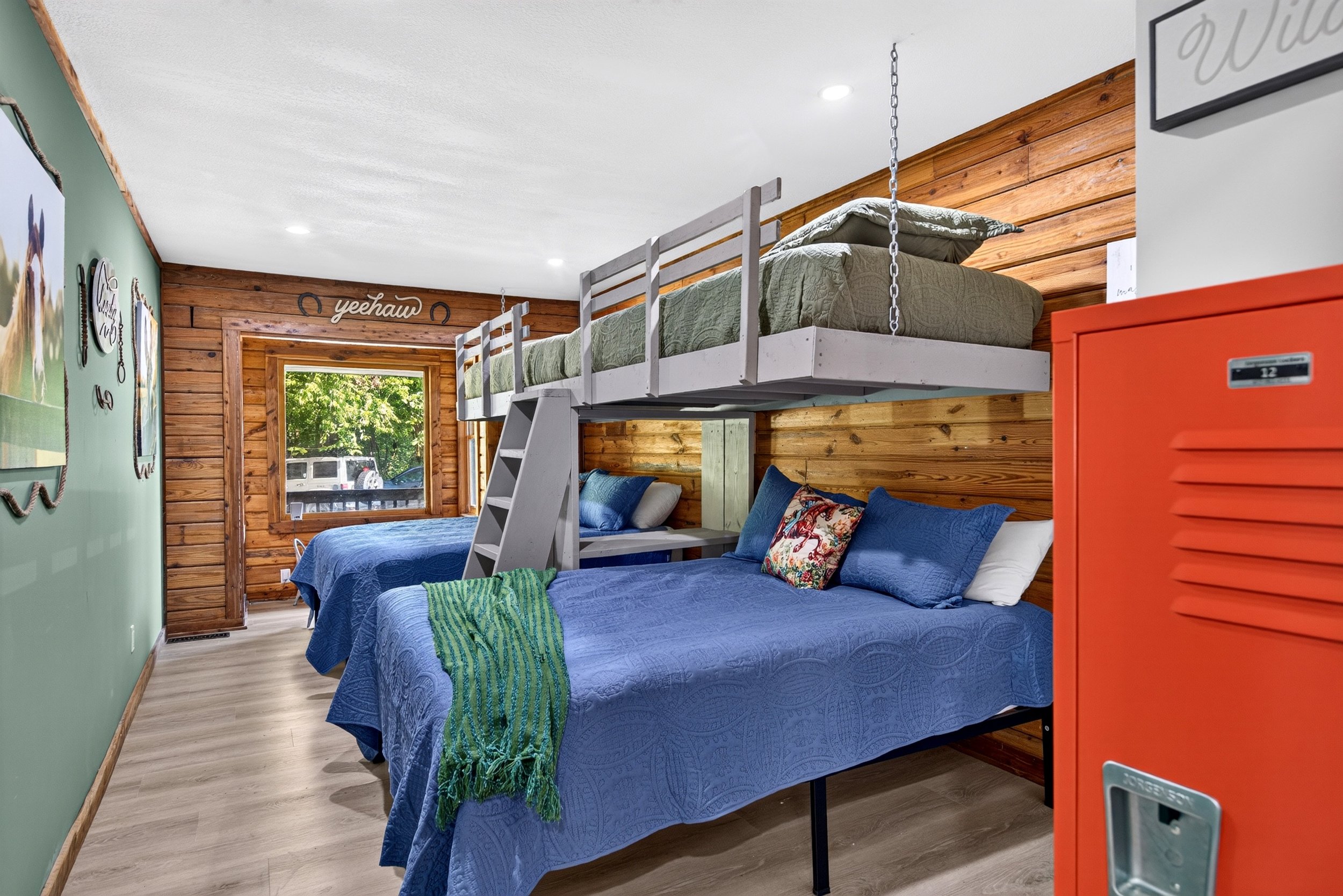 Bunk room at Refuge Ranch with two queen beds below and two twin bunks above, colorful bedding, wooded paneled walls, and windows over looking the trees.
