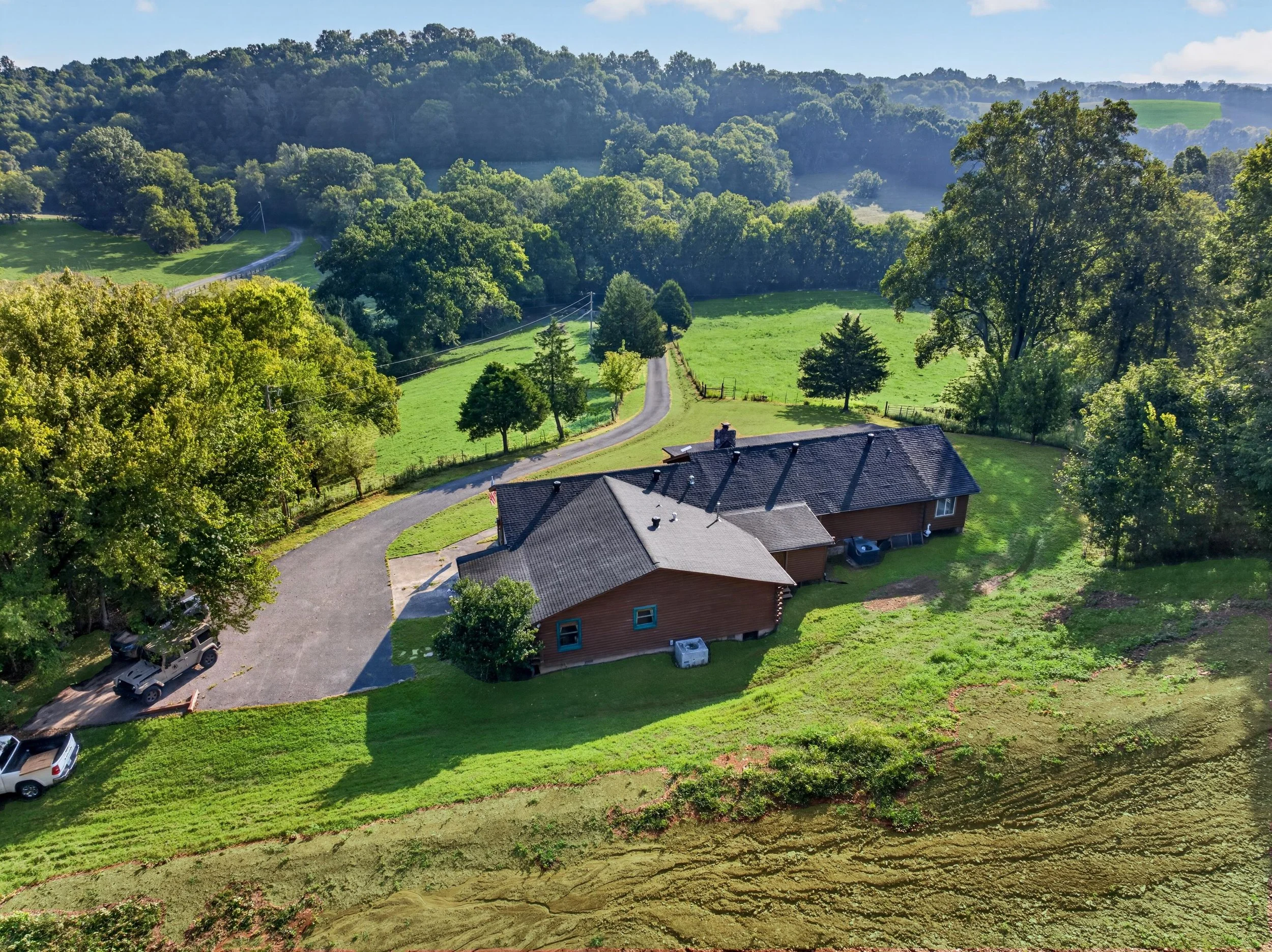 Aerial view of Refuge Ranch surrounded by rolling green hills and trees, with private driveway leading to the secluded retreat.