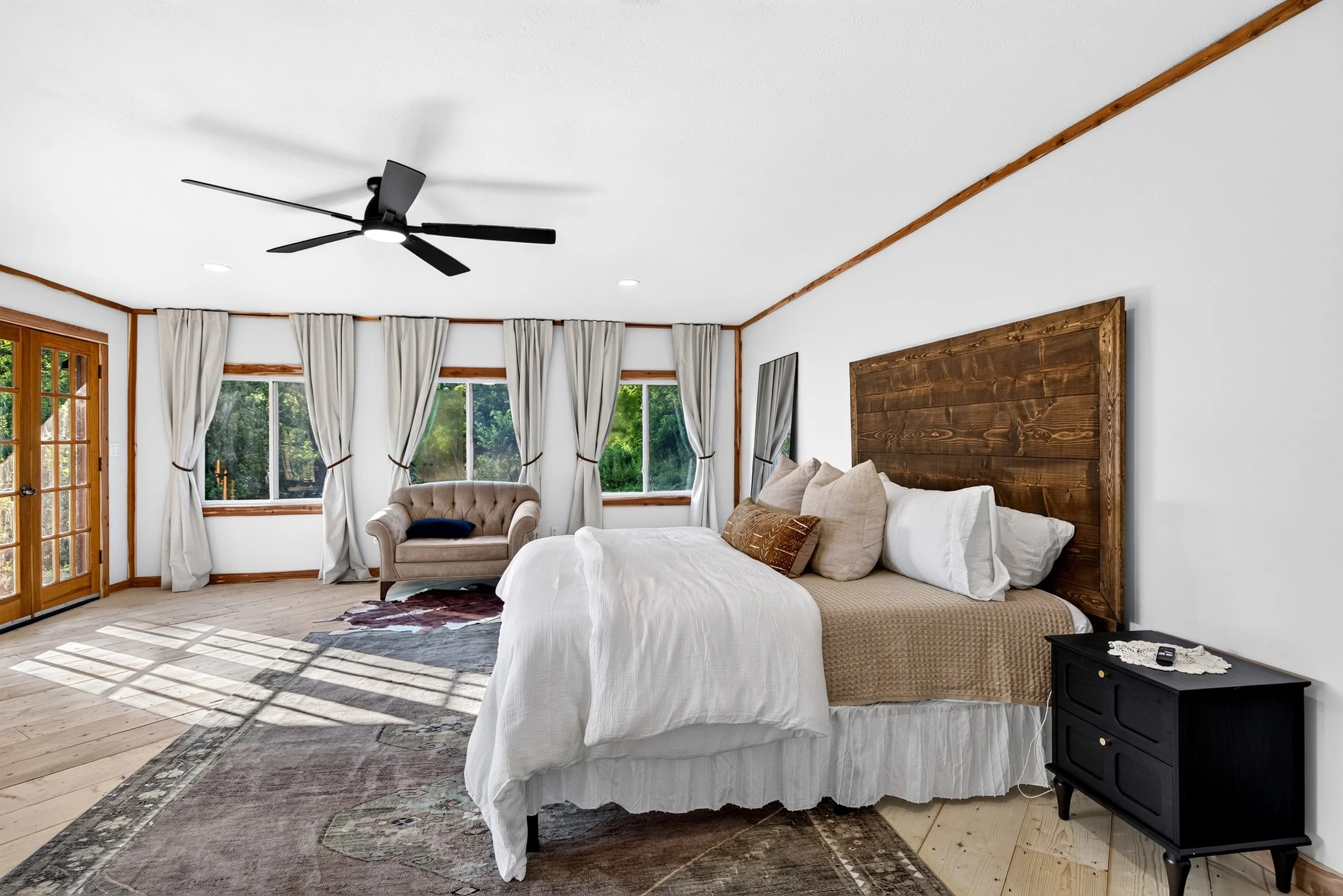 Primary suite at Refuge Ranch with a king size bed, large windows, beige curtains, warm wood headboard comfortable seating , and plenty of natural light. wake to sunrise views in  the morning. 