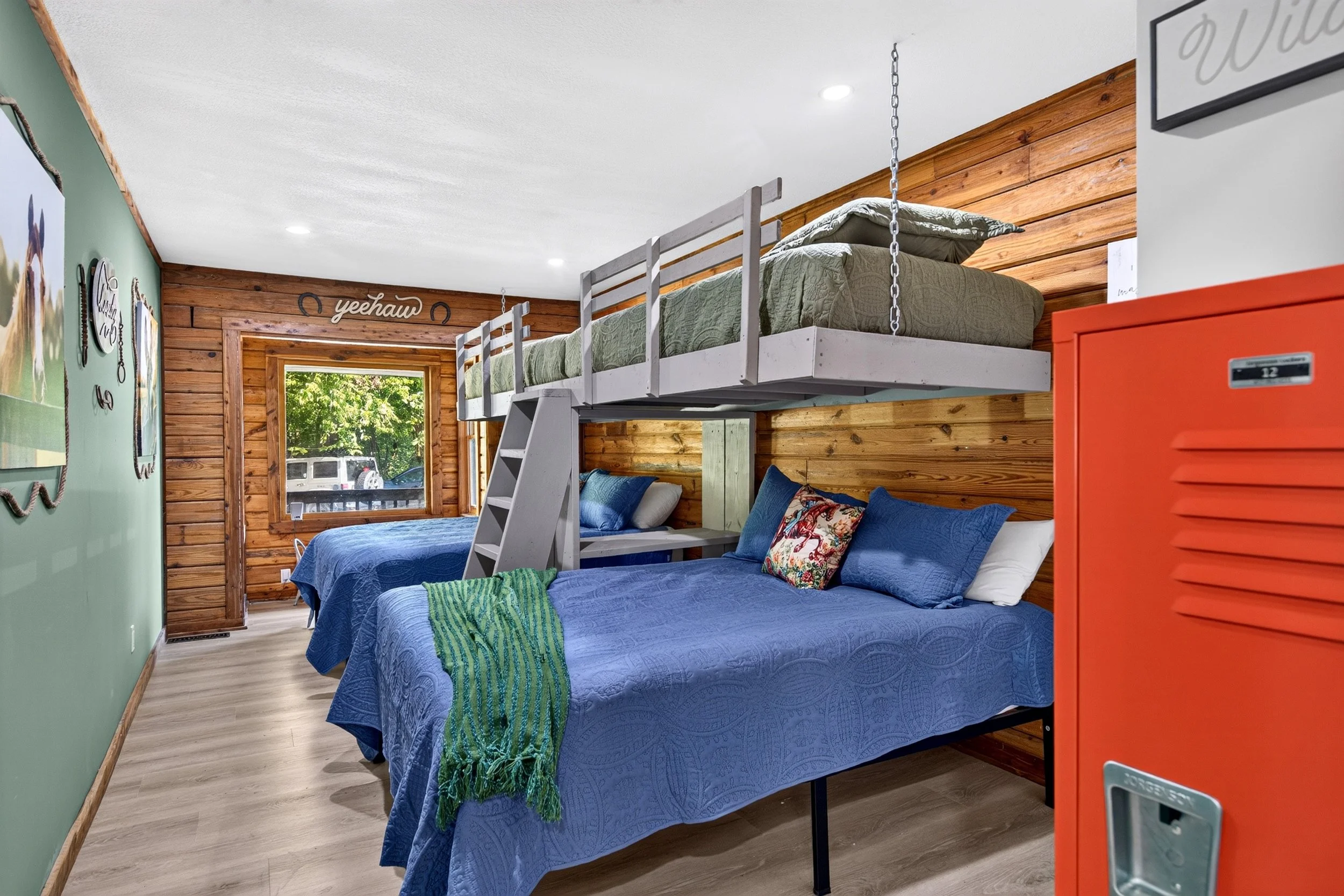Bunk room at Refuge Ranch with two queen beds below and two twin bunks above, colorful bedding, wooded paneled walls, and windows over looking the trees.