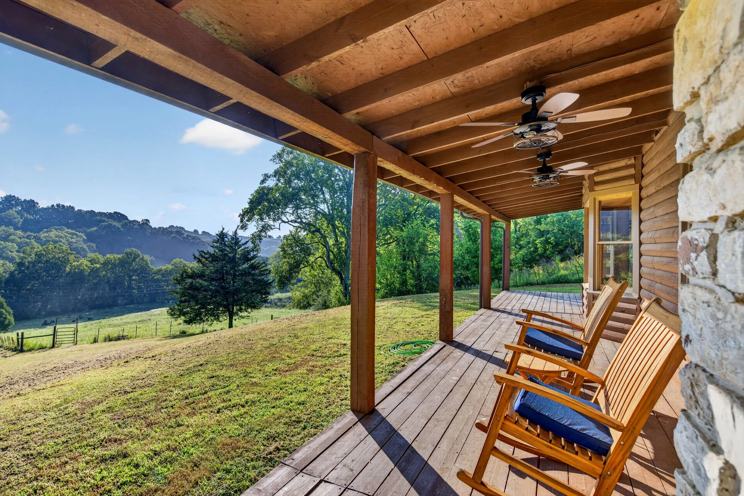 Covered wooden porch at Refuge Ranch with chairs overlooking green fields, mature trees, and rolling Tennessee countryside.