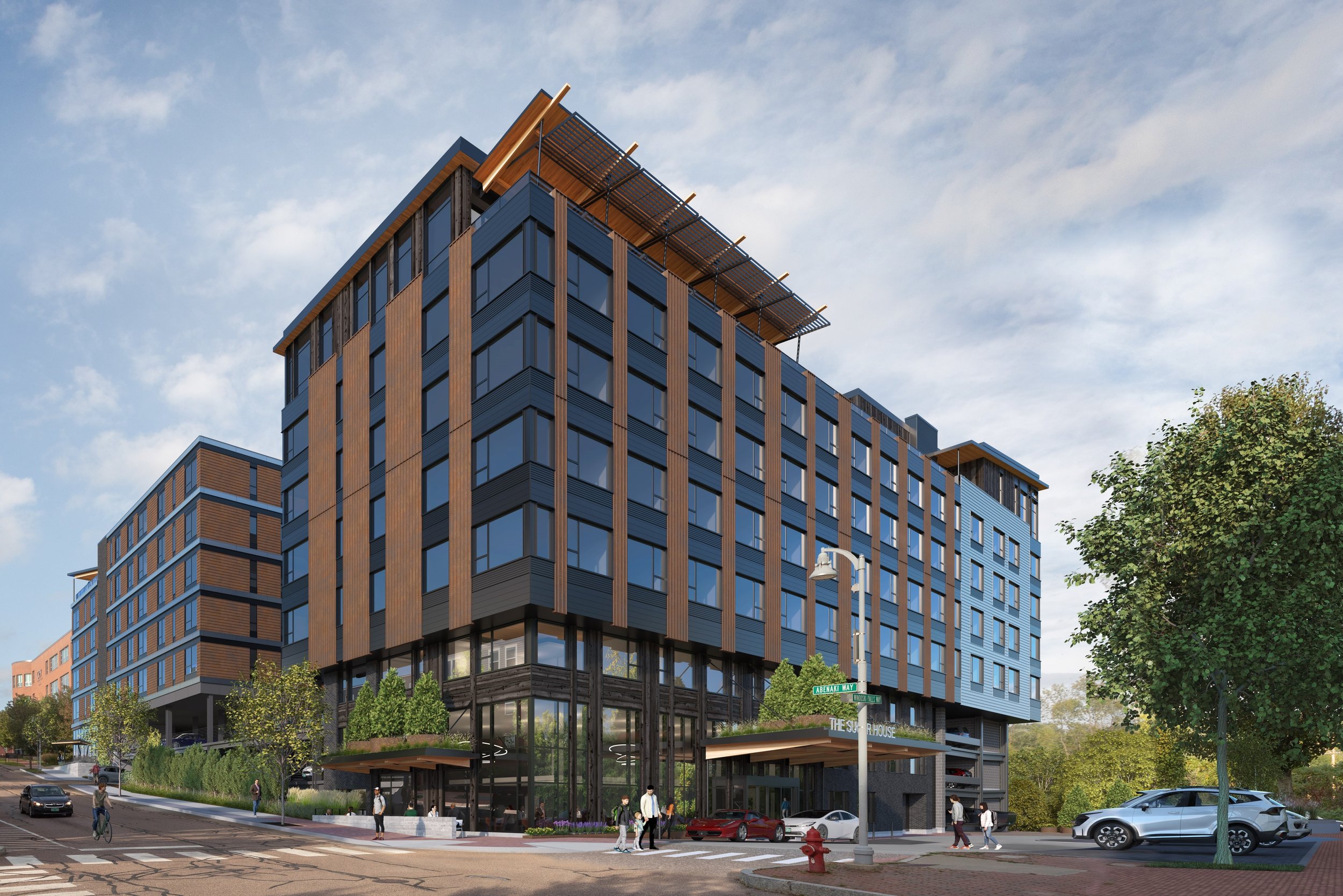 The Sugar House Hotel. A modern multi-story building with large glass windows and wooden paneling. Pedestrians are walking by on the sidewalk, and cars are parked in front. Trees and street signs are visible, with a blue sky and some clouds overhead.