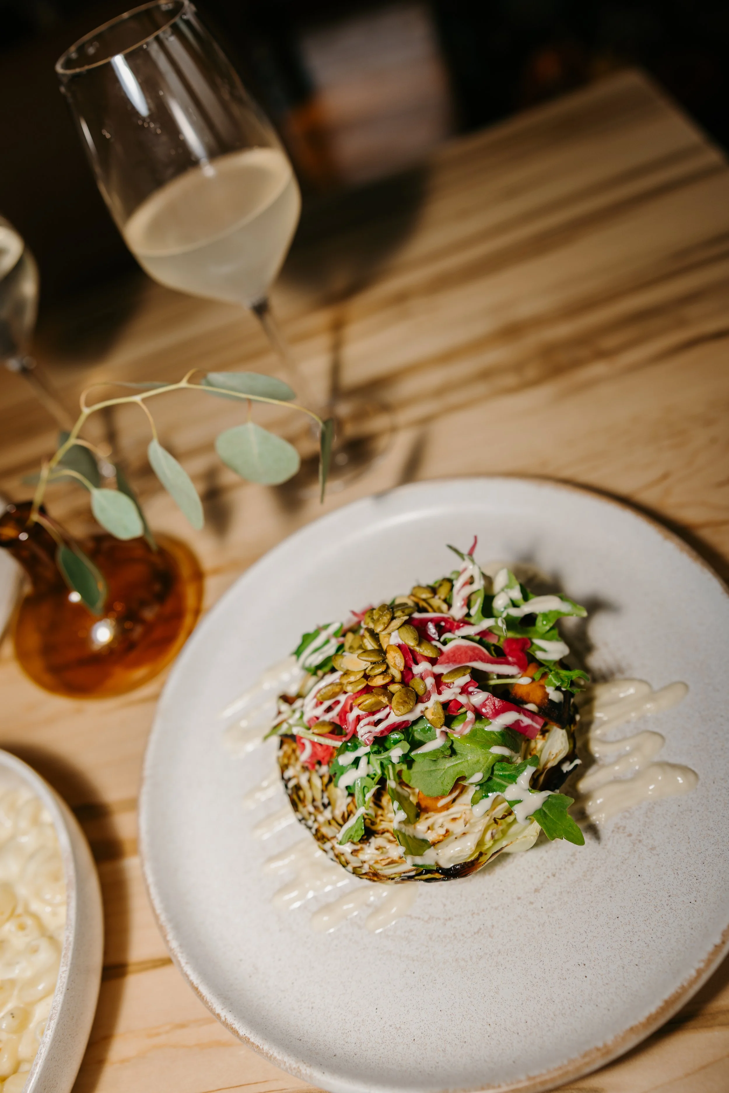 A layered salad with greens, sliced vegetables, seeds, and drizzled dressing on a white plate.
