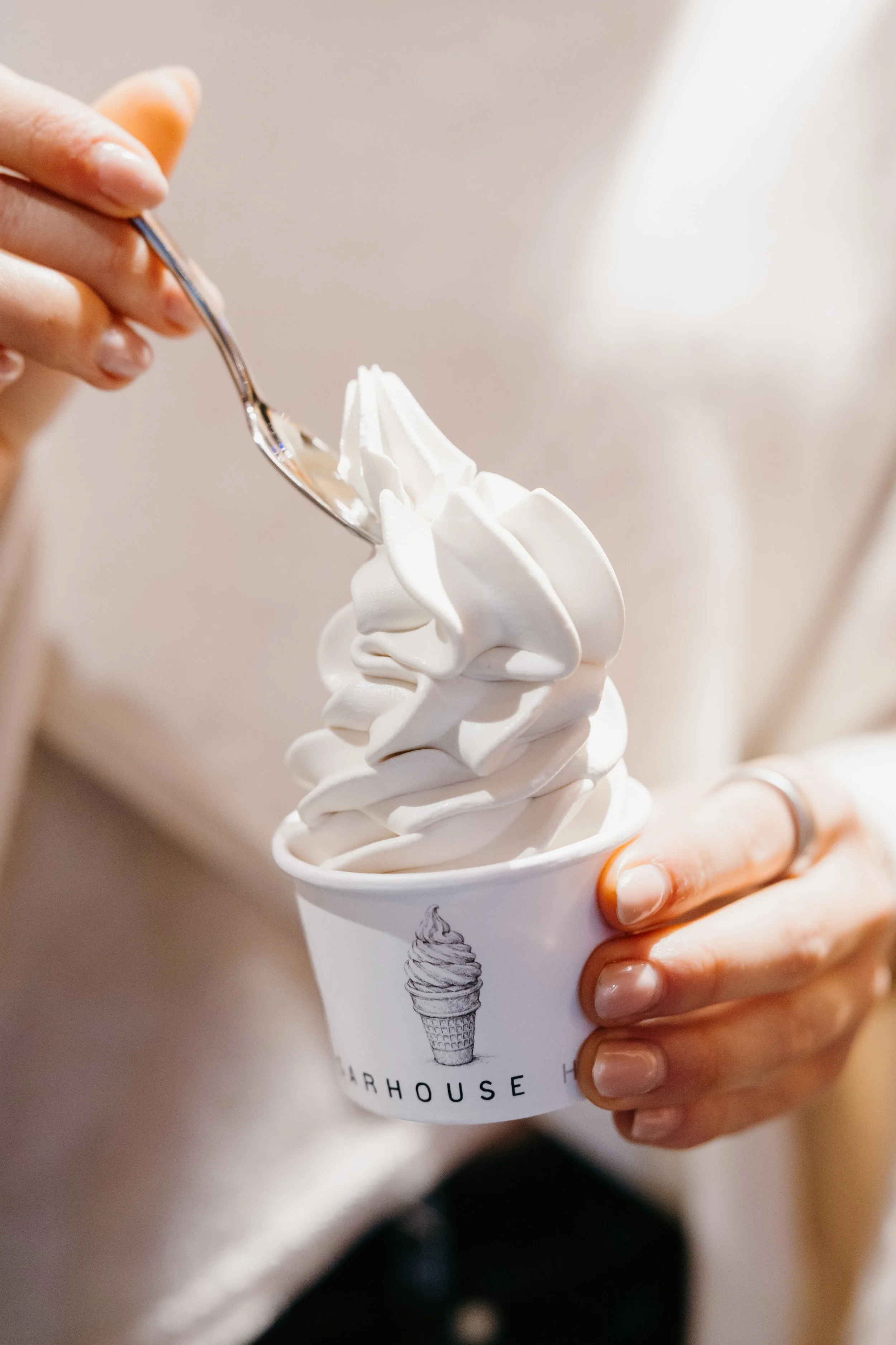A person holding a cup of soft serve vanilla ice cream with a spoon in hand, about to take a bite.