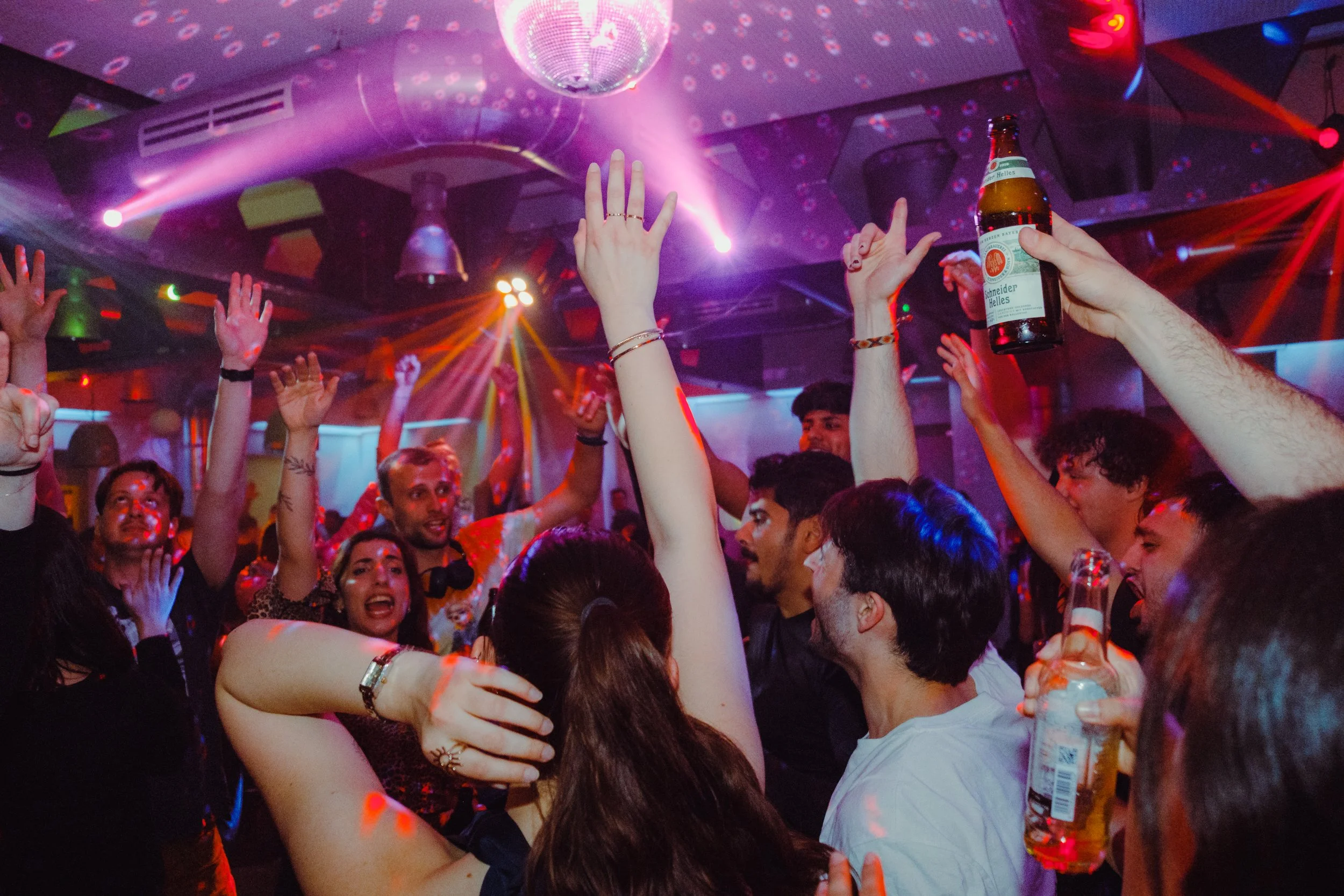 People dancing and having fun at a nightclub with colorful lights and a disco ball.