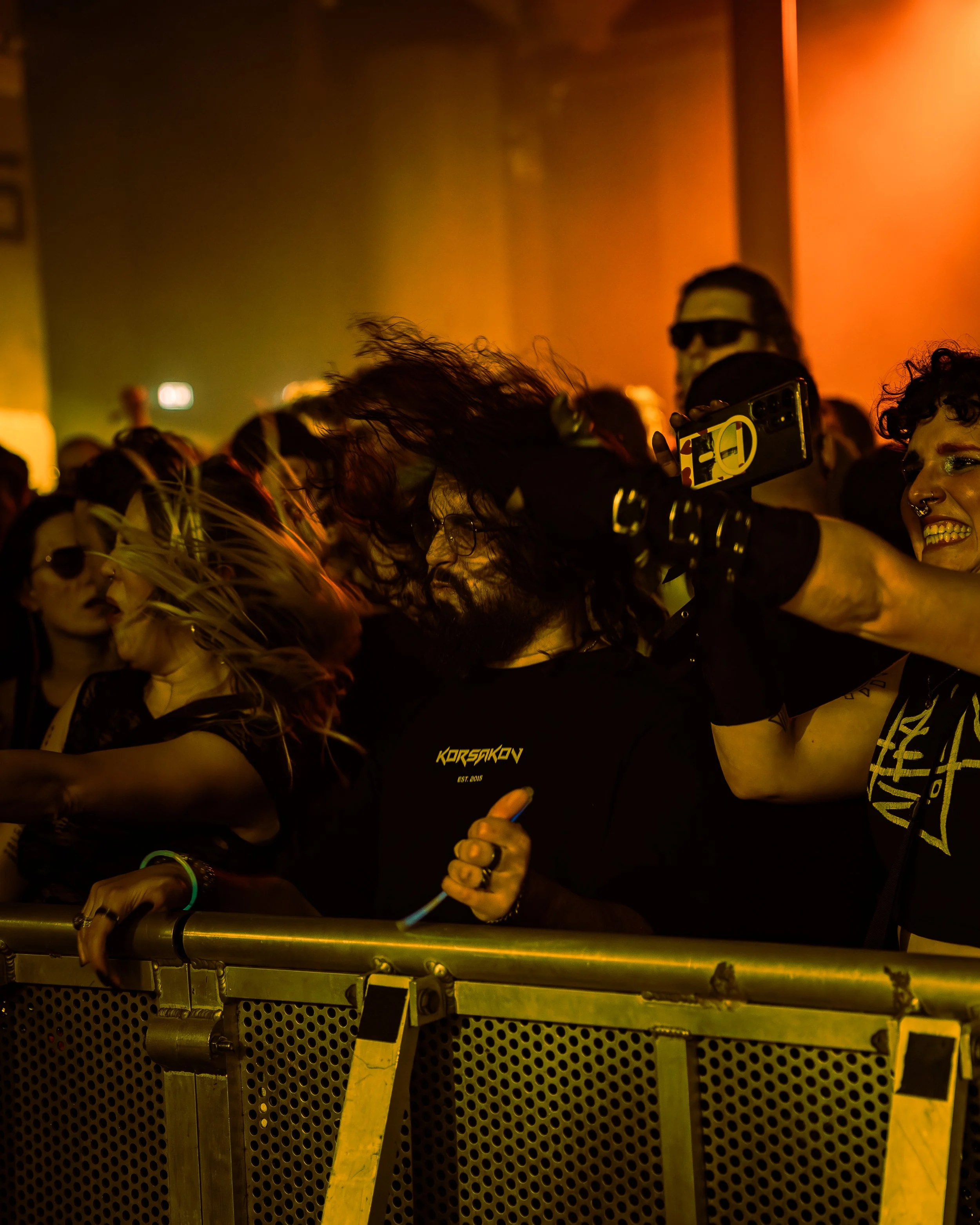 People dancing at a party with orange lighting, one person holds a smartphone and takes a selfie, others are smiling and enjoying the music.