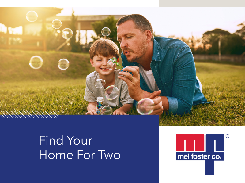 A man and a young boy lying on the grass outdoors, blowing soap bubbles together during sunset