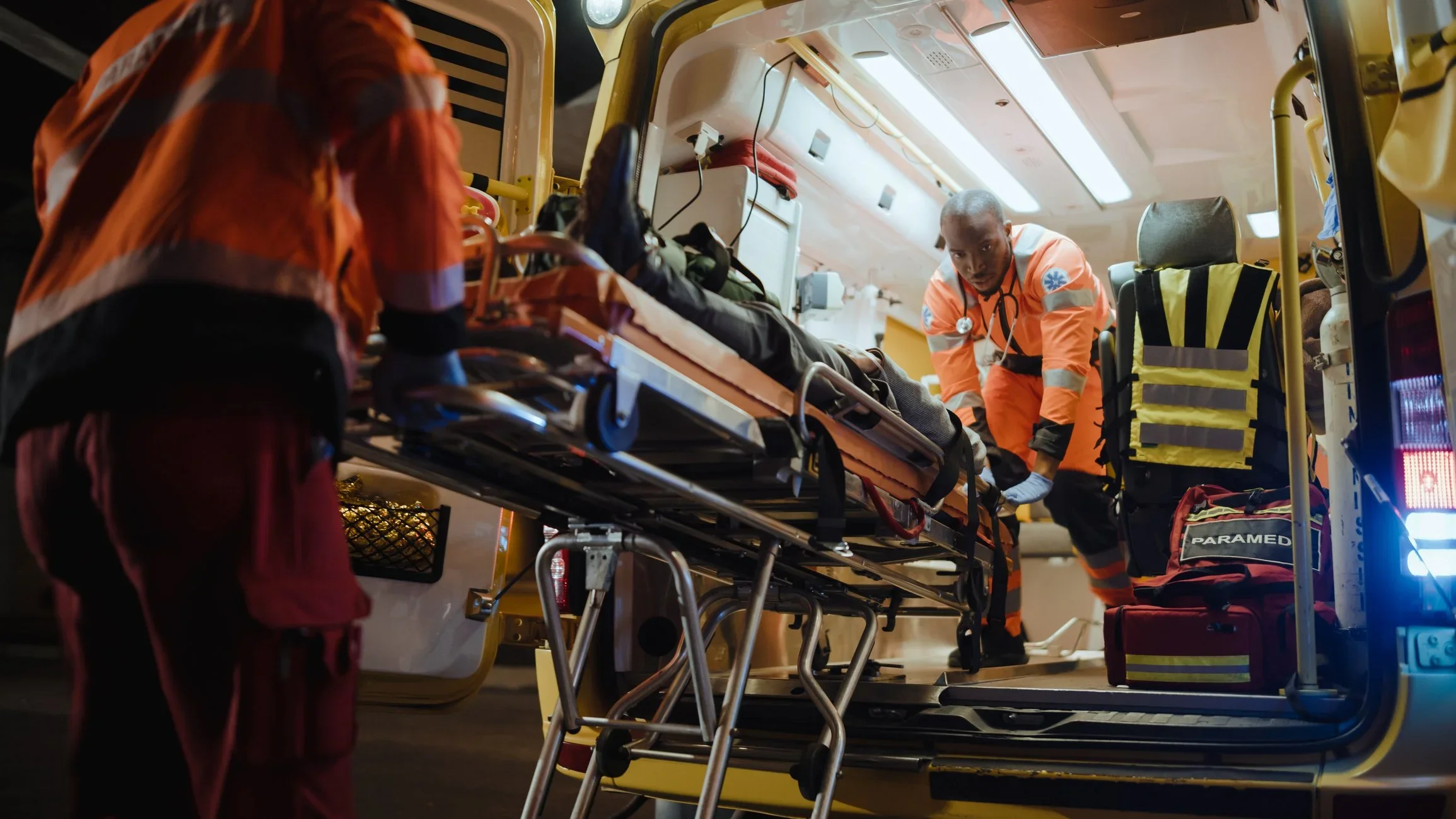 Emergency medical personnel attending to a patient on a stretcher inside an ambulance, with medical equipment nearby.