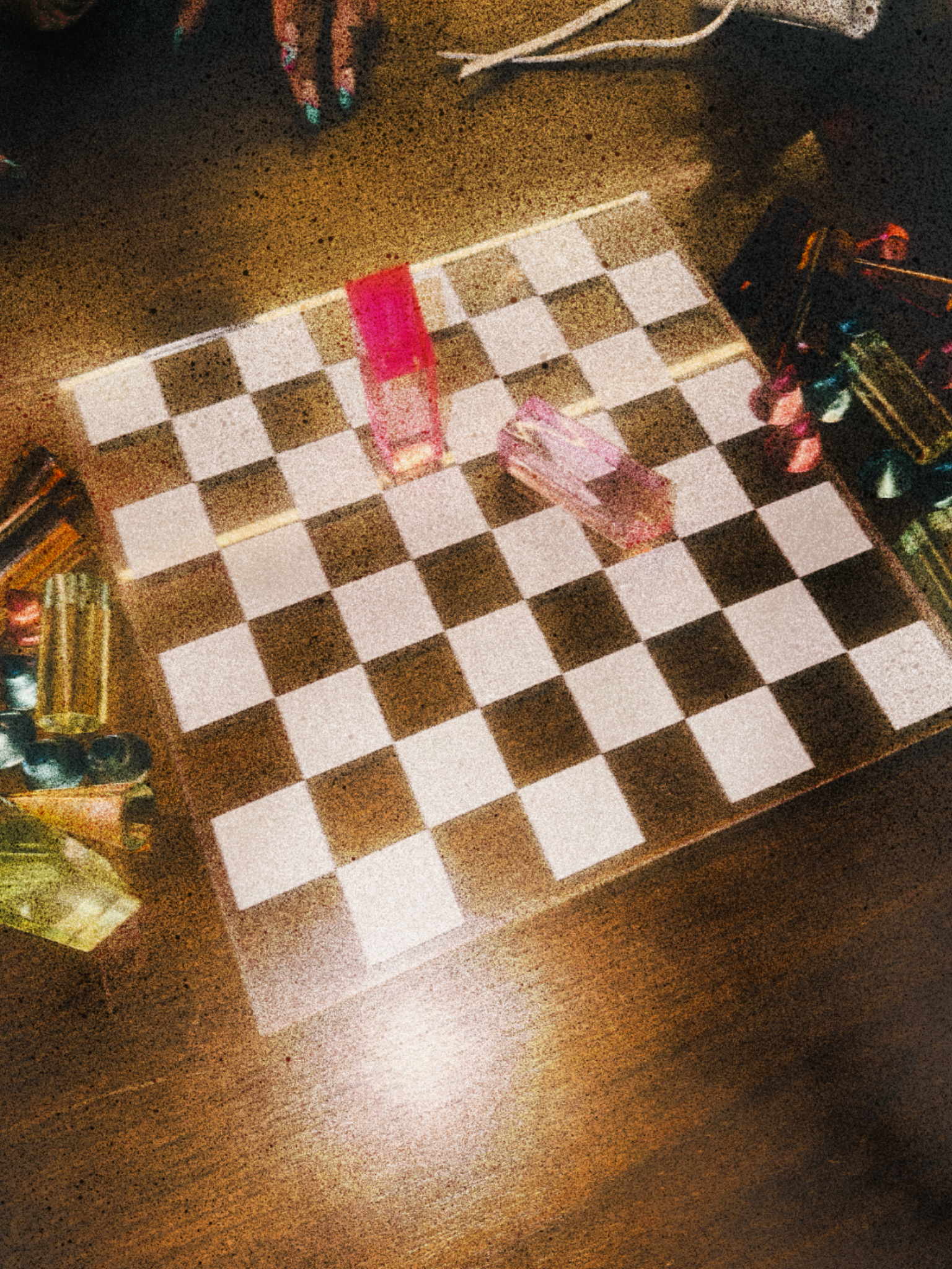A chessboard on a wooden surface with two pink acrylic cubes and several colored pencils nearby.