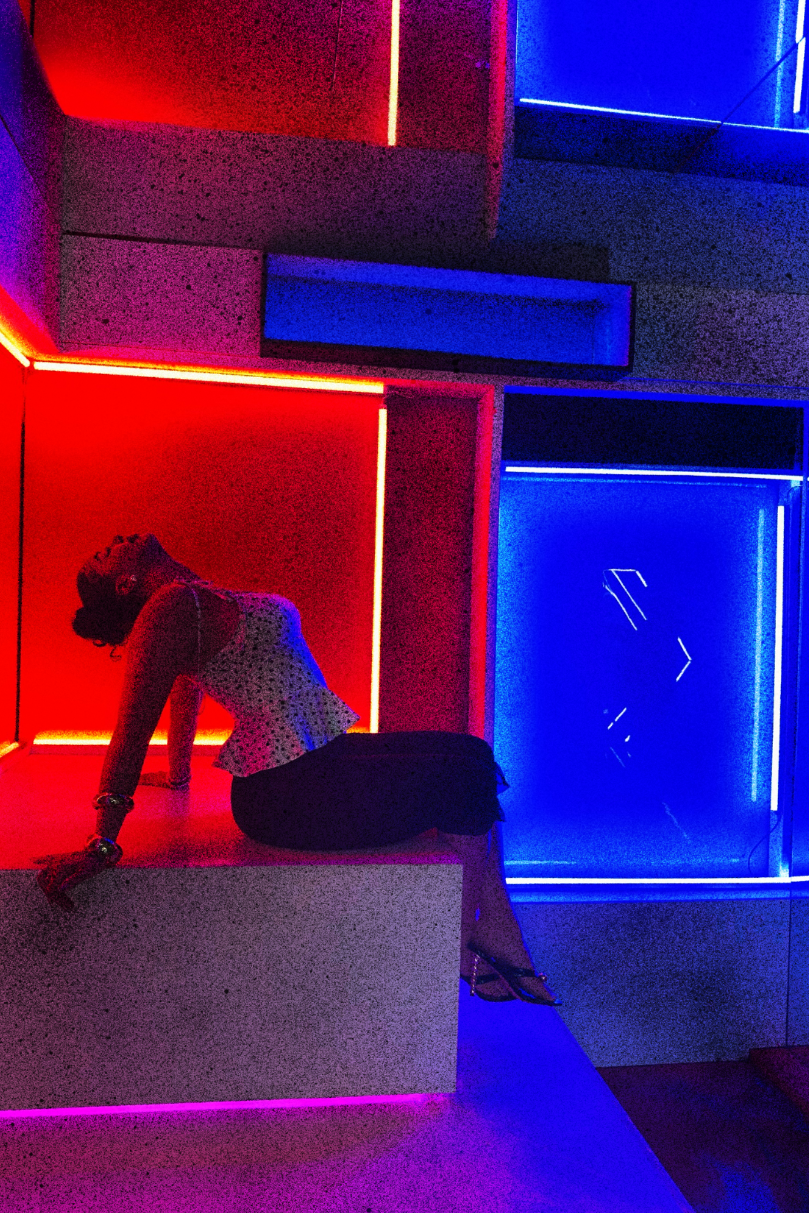 A woman poses in a dark room with colorful neon blue, red, purple and pink lights outlining the space, creating a vibrant atmosphere.