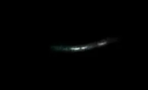 A faint, elongated light in the dark, possibly a distant celestial object or a streak of light in the night sky.