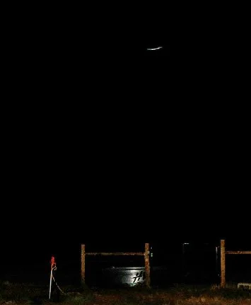 Nighttime scene with a crescent moon, a propane tank, and a fence.