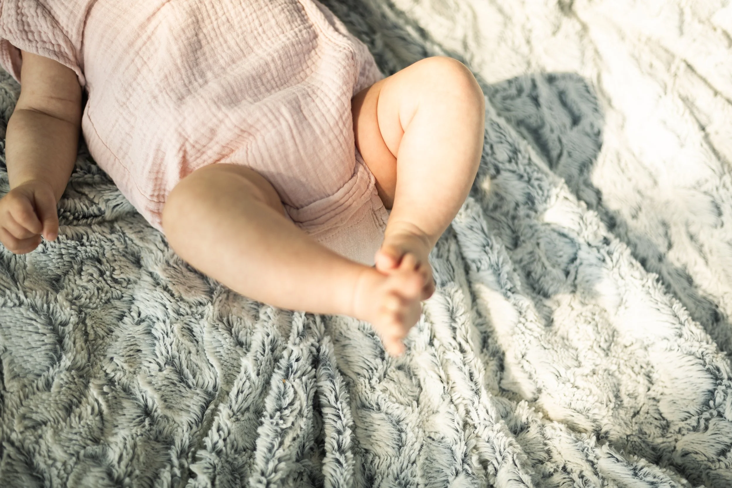 Un bébé allongé sur un tapis en peluche, vêtu d'un pyjama rose, entouré d'un environnement doux et confortable.