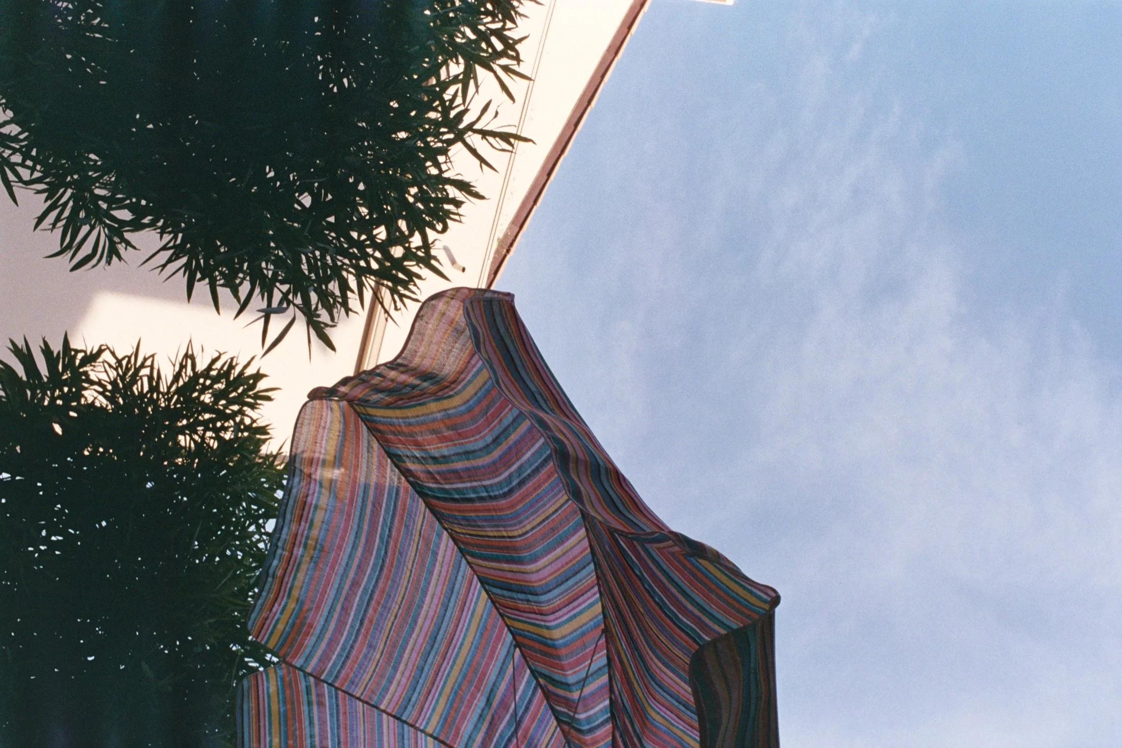 Un parasol coloré avec des rayures multicolores sous un ciel clair, entouré d'arbustes ou d'arbres