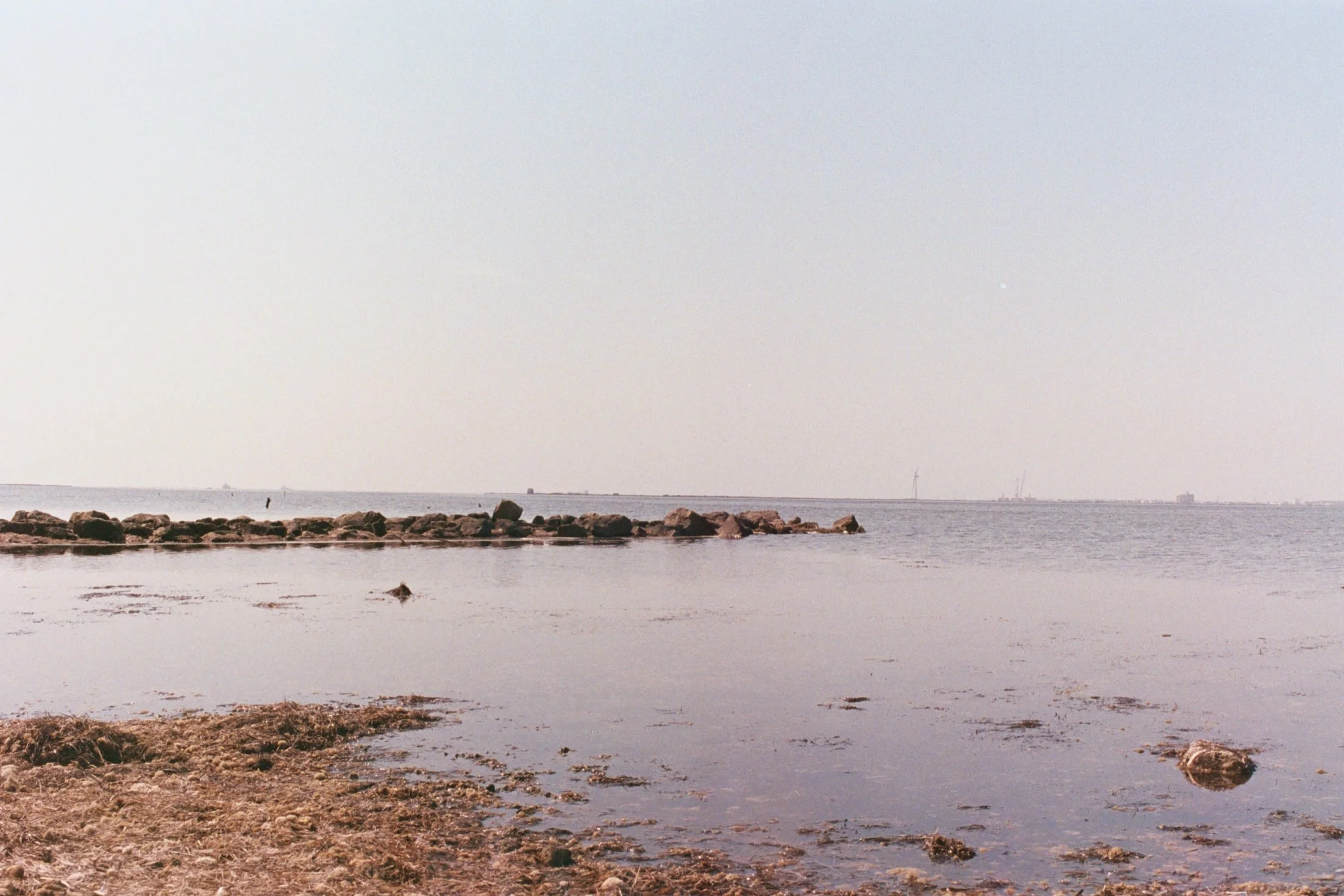 Plage rocheuse avec eau calme et horizon lointain, ciel clair.