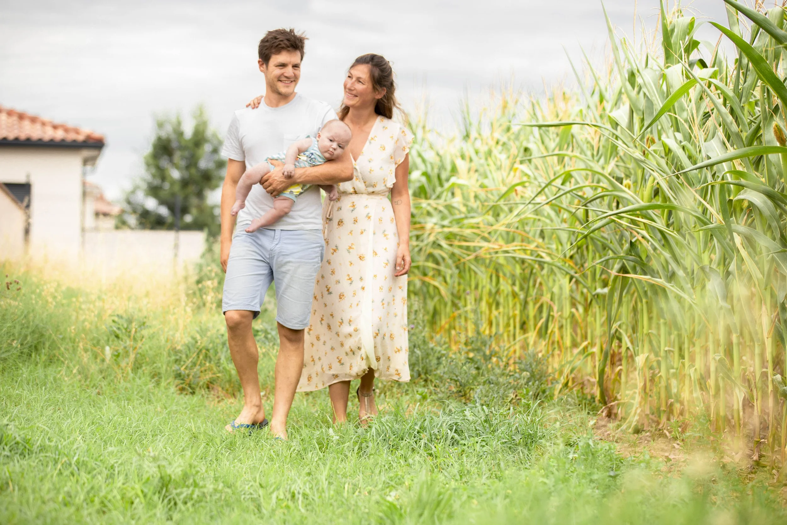 Famille marchant dans un champ de maïs, un homme tenant un bébé, une femme souriante.