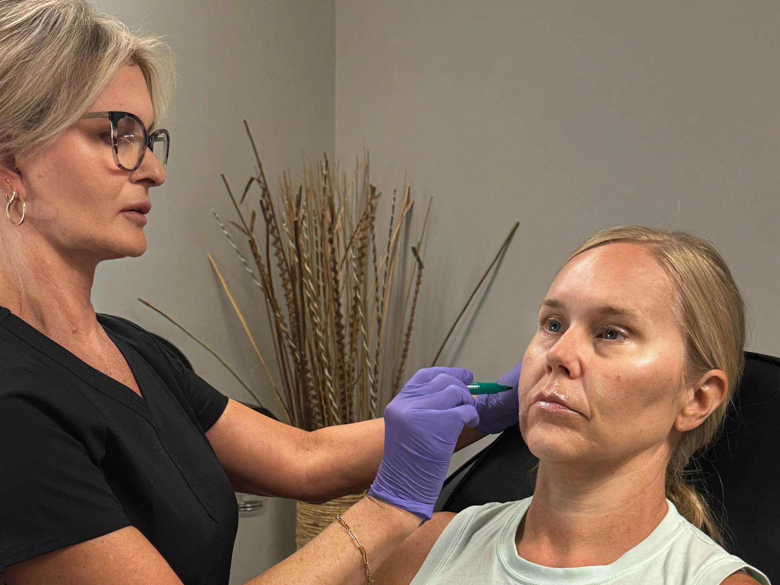 A woman receiving a facial injection administered by a healthcare professional wearing purple gloves. The woman has blonde hair and blue eyes at Rejuvenate Wellness in Florence Kentucky