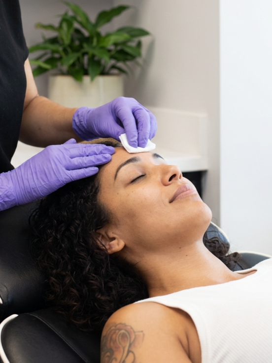 A woman receiving a facial treatment from an esthetician wearing purple gloves at Rejuvenate Wellness in Florence Kentucky