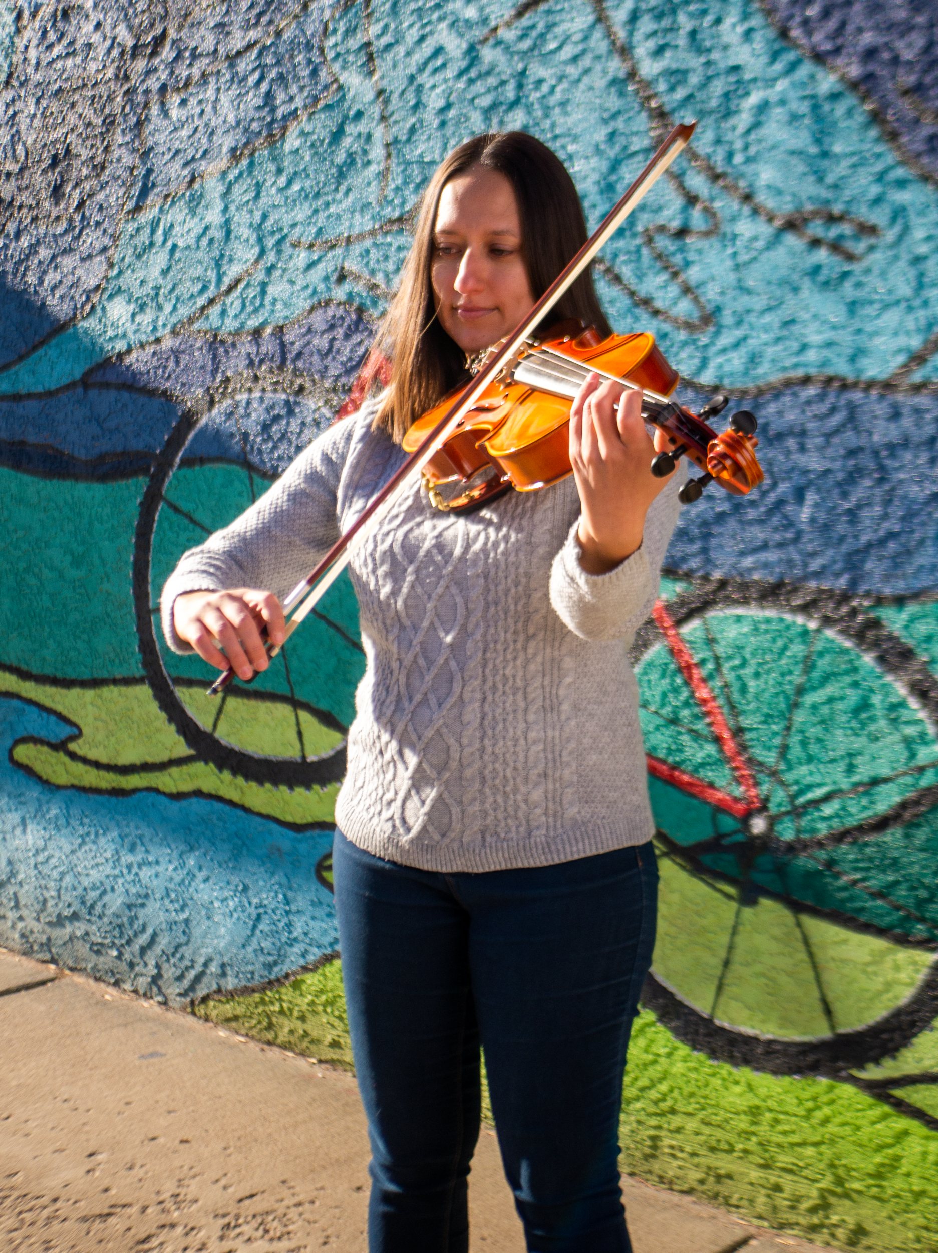A woman playing a violin in front of a colorful mural.