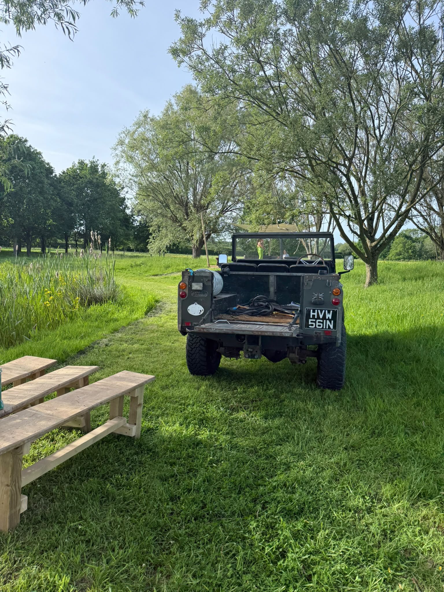 A black utility vehicle parked on a grassy field surrounded by trees under a clear blue sky.