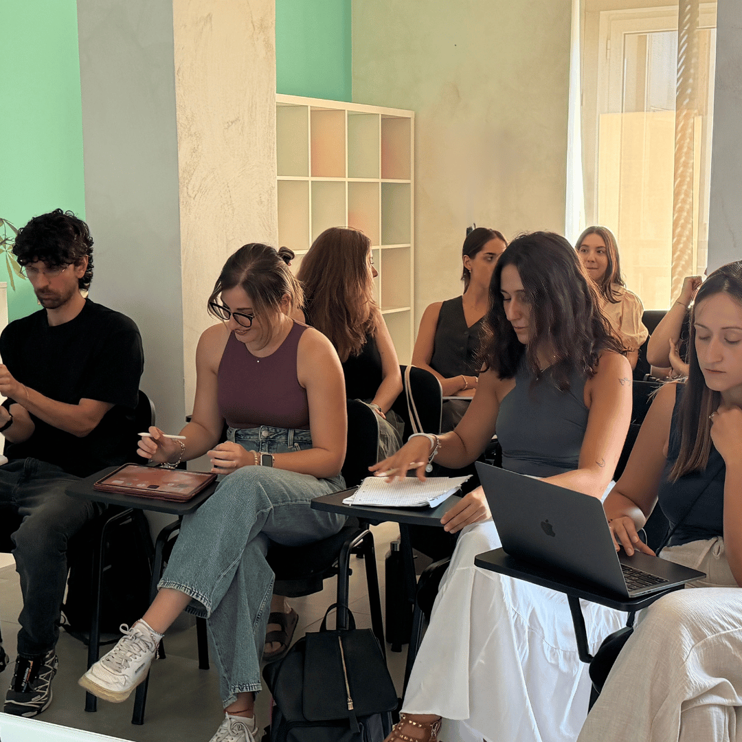 Gruppo di persone sedute in una sala, alcune con laptop e quaderni.