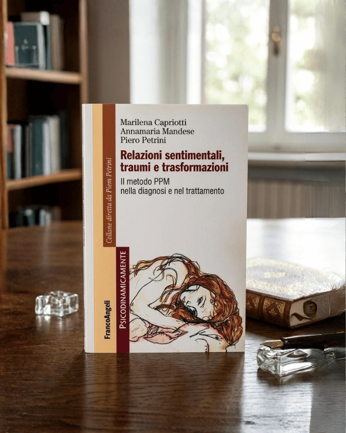 Libro intitolato "Relazioni sentimentali, traumi e trasformazioni" su un tavolo vicino a una finestra, con libri e oggetti in vetro intorno.