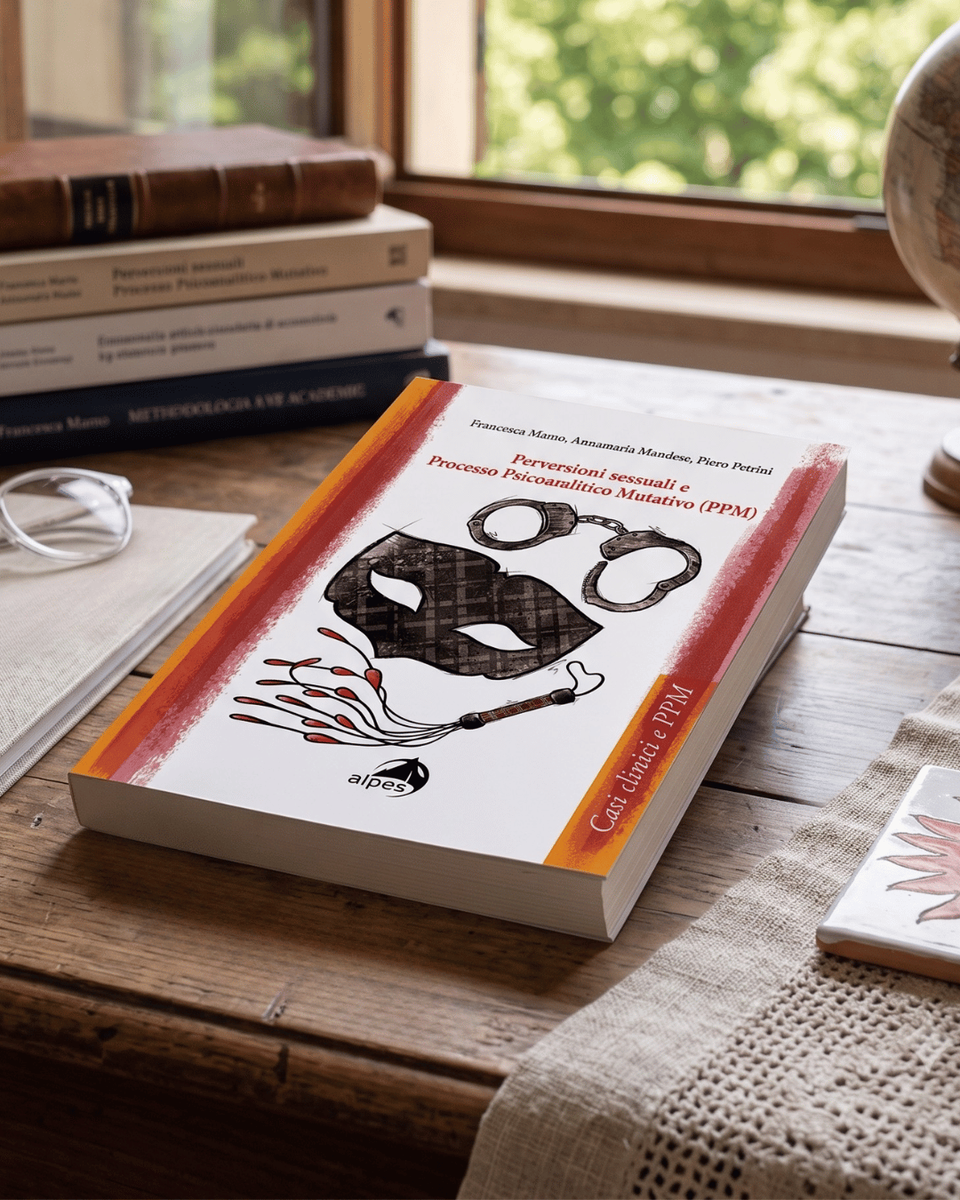 Libro di fronte a una finestra con altri libri impilati, occhiali, un quaderno, e una bussola in un ambiente di studio o ufficio.