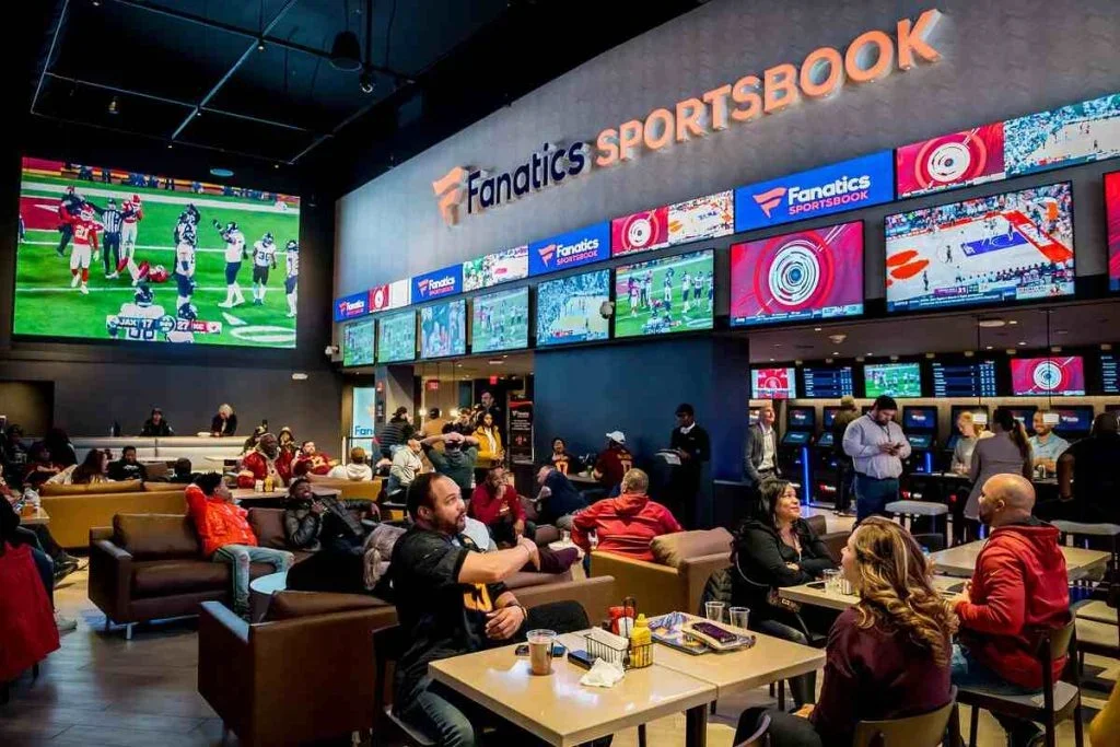 Sportsbook bar and lounge with people watching football on multiple screens, large TVs, and betting terminals at Fanatics Sportsbook