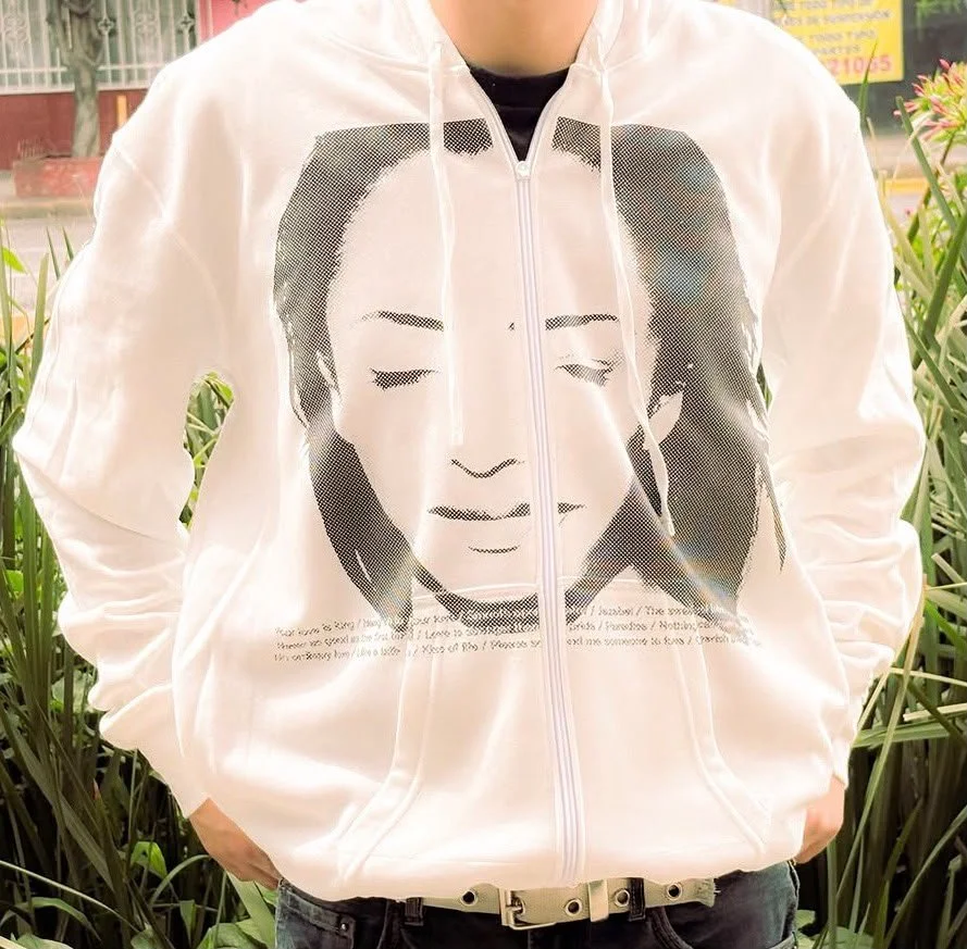 Person wearing a white zip-up hoodie featuring a large black and white graphic portrait of a woman with closed eyes and long hair.