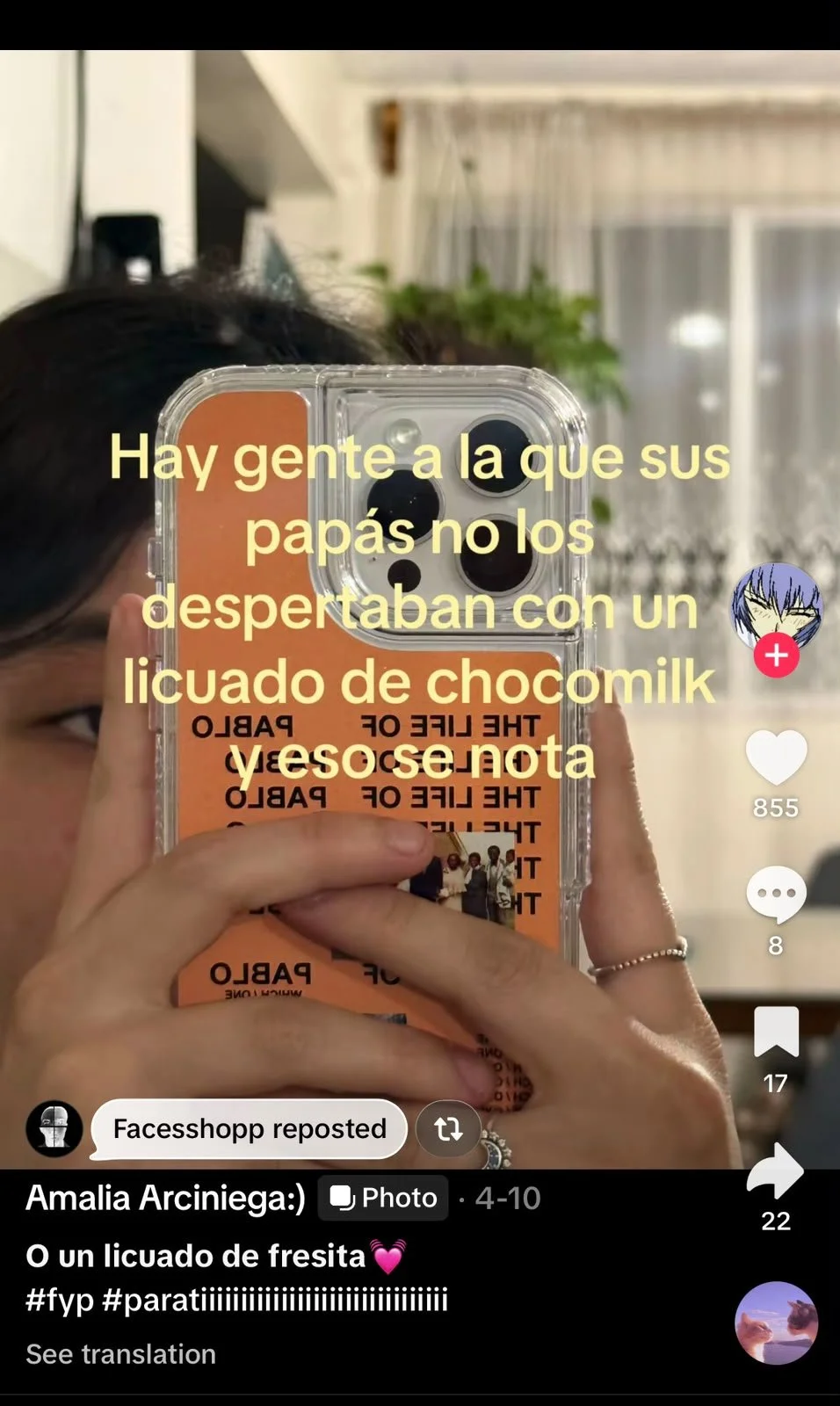 A woman taking a mirror selfie with a phone in a transparent case, with a background of curtains and plants. Overlaid text in Spanish mentions people who wake up to a frappuccino or a milkshake.