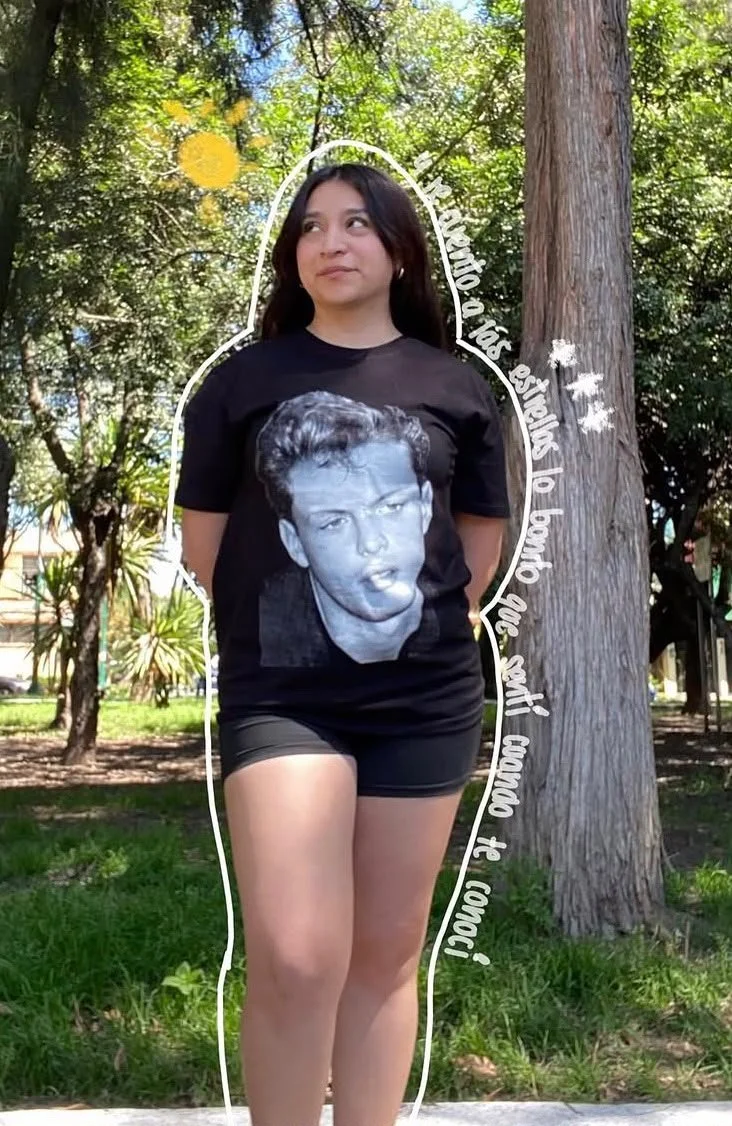 Woman standing outdoors in front of trees, wearing a black t-shirt with a large grayscale image of a young man, with handwritten-style text around her that reads, "La memoria de mis hermanos no se borra, las mil calles no pueden to con nosotros".