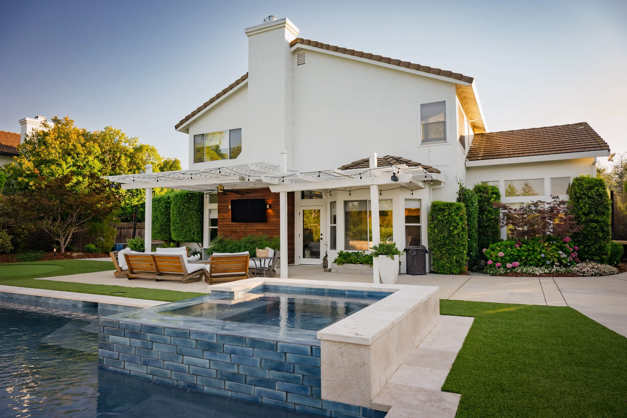 A modern white house with a backyard pool area, surrounded by green landscaping and outdoor seating.