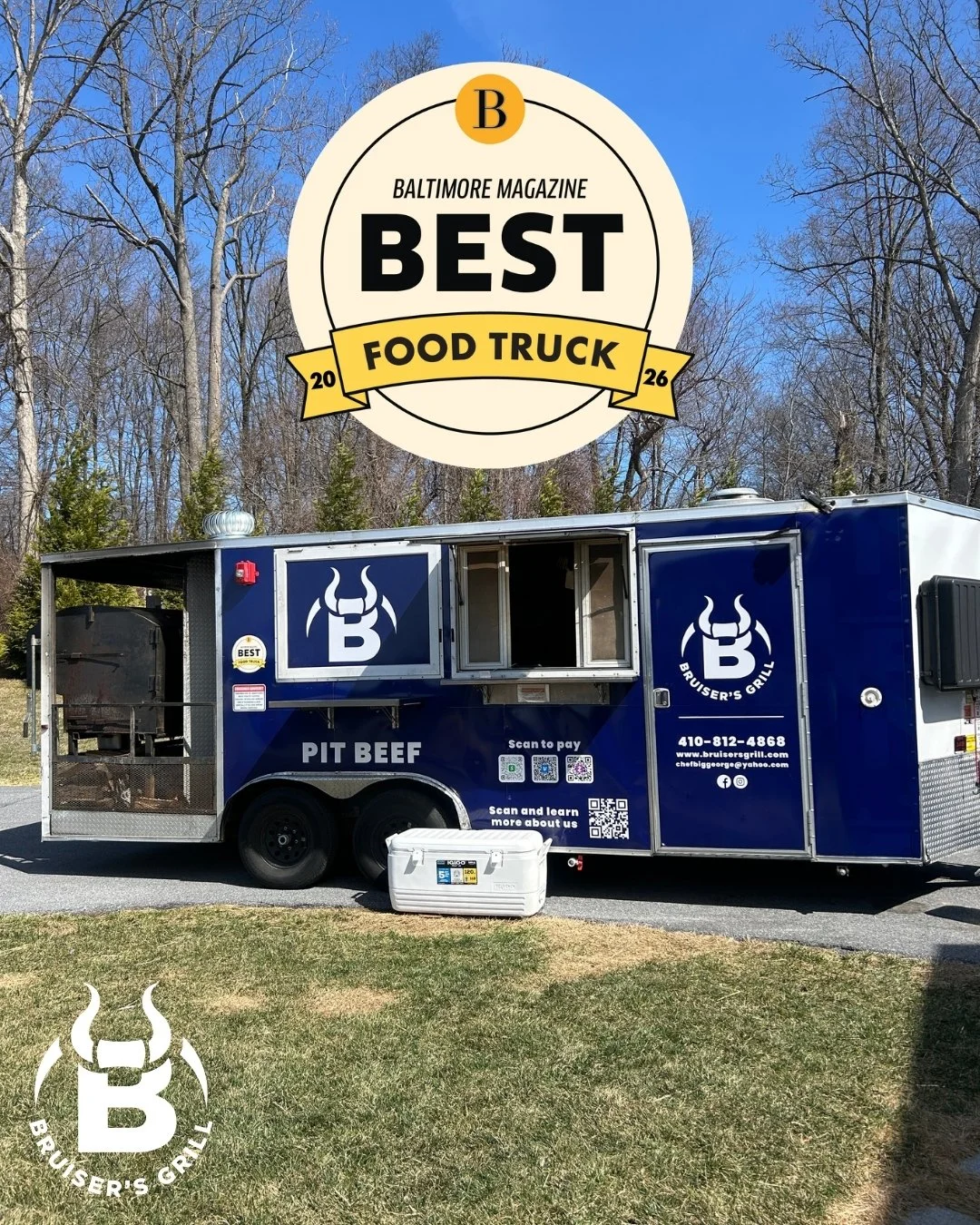 Blue food truck with 'Pit Beef' signage and a logo featuring a stylized bull's horns and the letter B, parked on a grassy area with trees and a clear blue sky in the background.