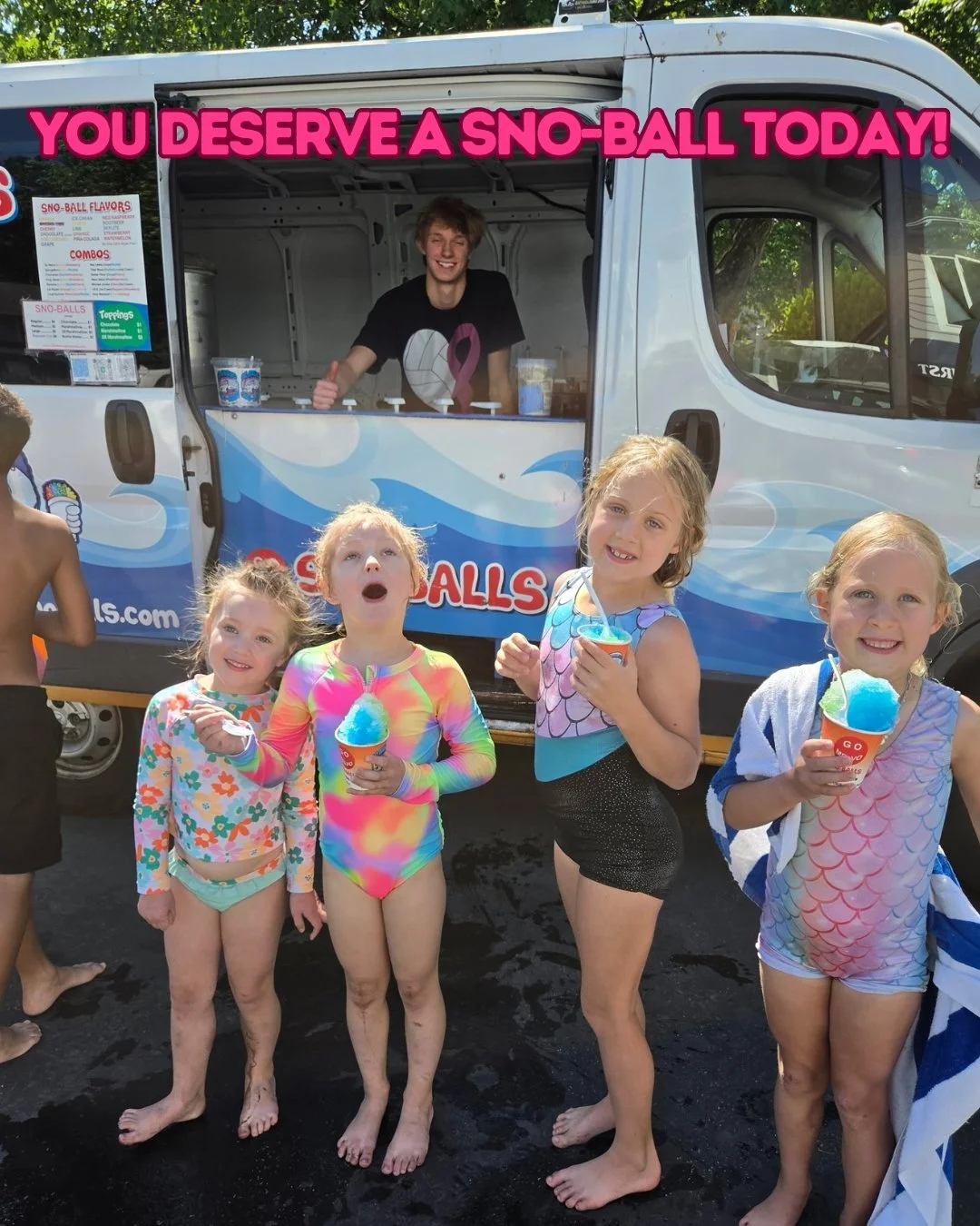 A group of four young girls in swimsuits holding colorful snow cones at a summer event, standing in front of a snow cone truck with a person inside giving a thumbs-up and smiling, with a banner above that says 'You deserve a sno-ball today!'.