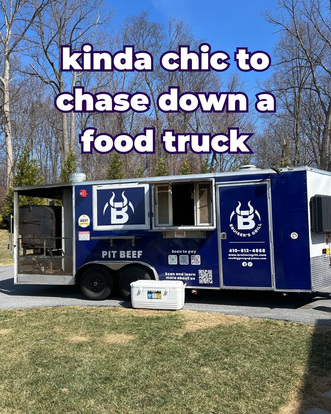 A blue food truck with logo and contact information, parked on a grassy area with trees in the background, advertising pit beef, with a white cooler in front.