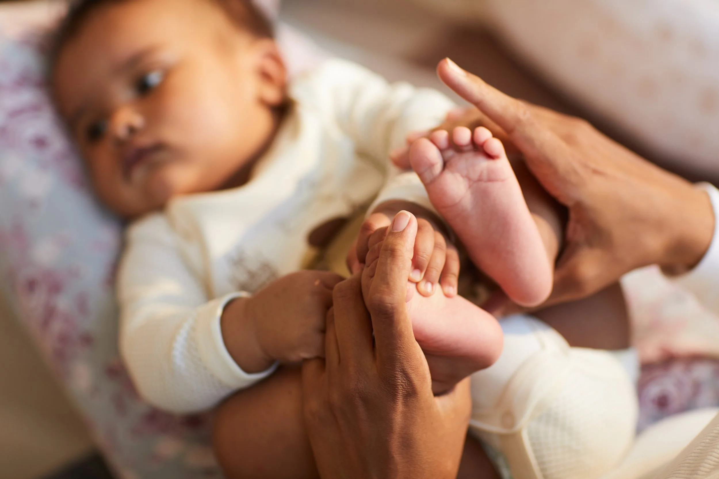 Close-up of a child lying down, holding hands with an adult.