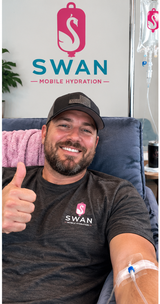 Man in a black t-shirt and cap giving a thumbs-up, sitting in a chair with medical IV in his arm, in front of a "SWAN Mobile Hydration" sign.