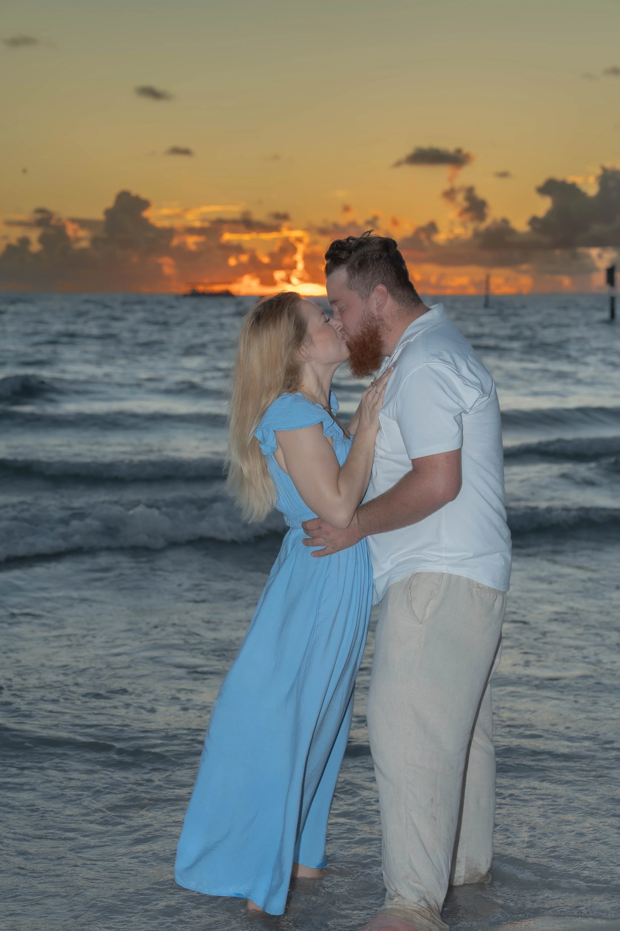 A couple kissing on the beach during sunset with the ocean behind them.